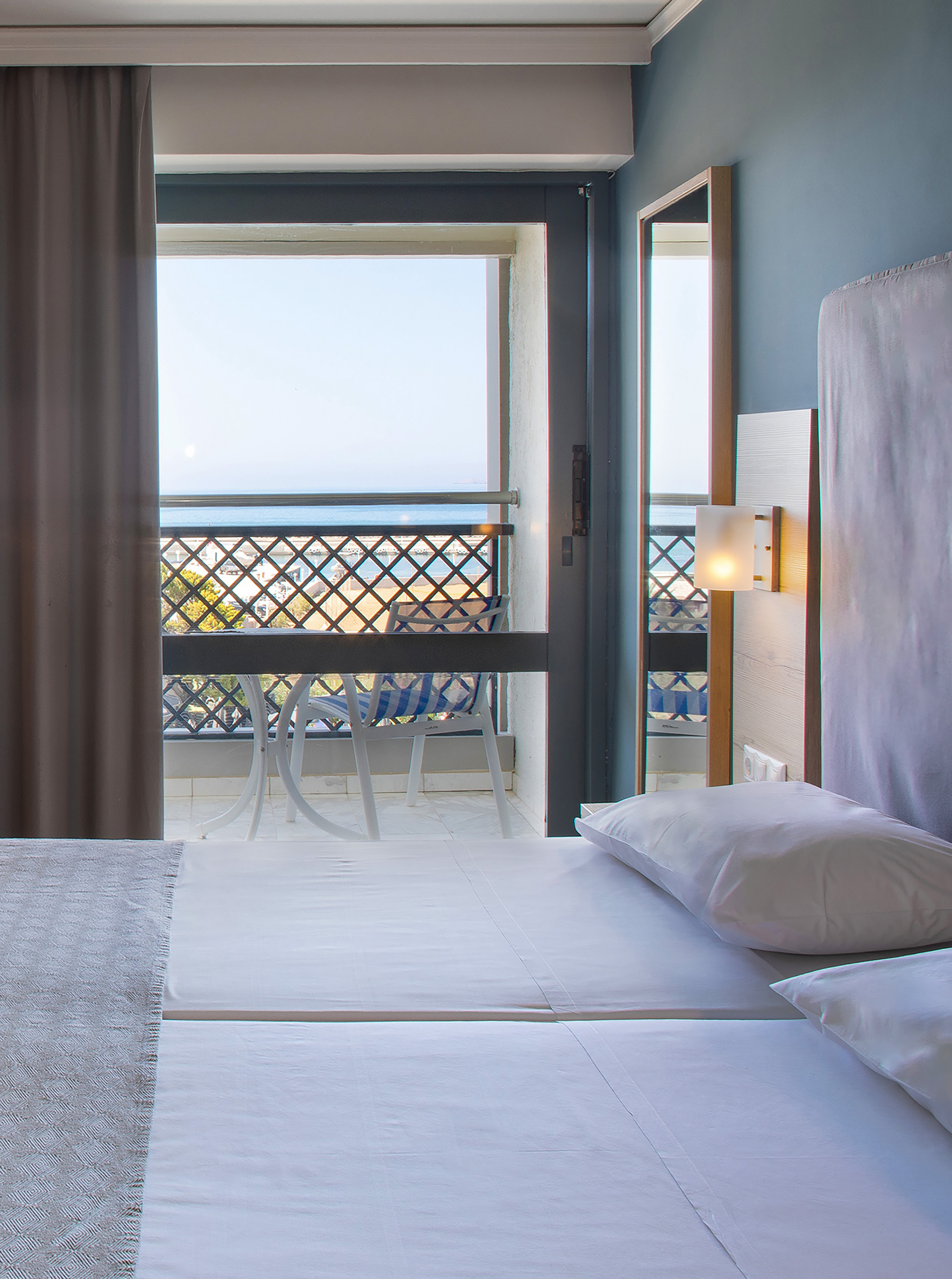 Hotel room with white bed, balcony, and ocean view.