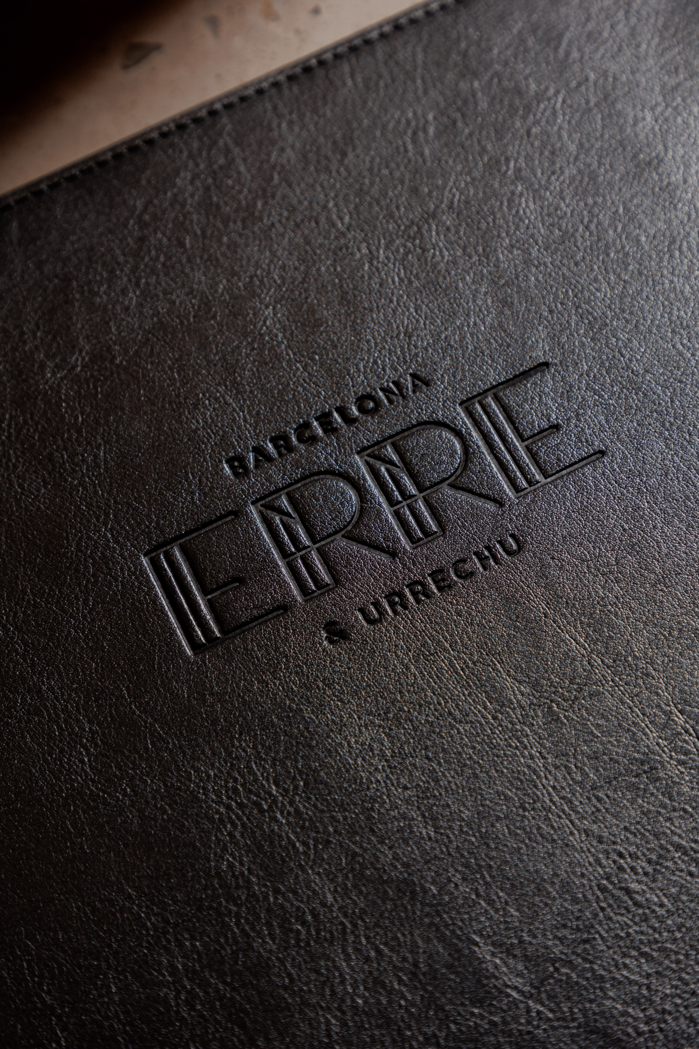 Embossed 'ERRE & URRECHU Barcelona' logo on dark textured leather.