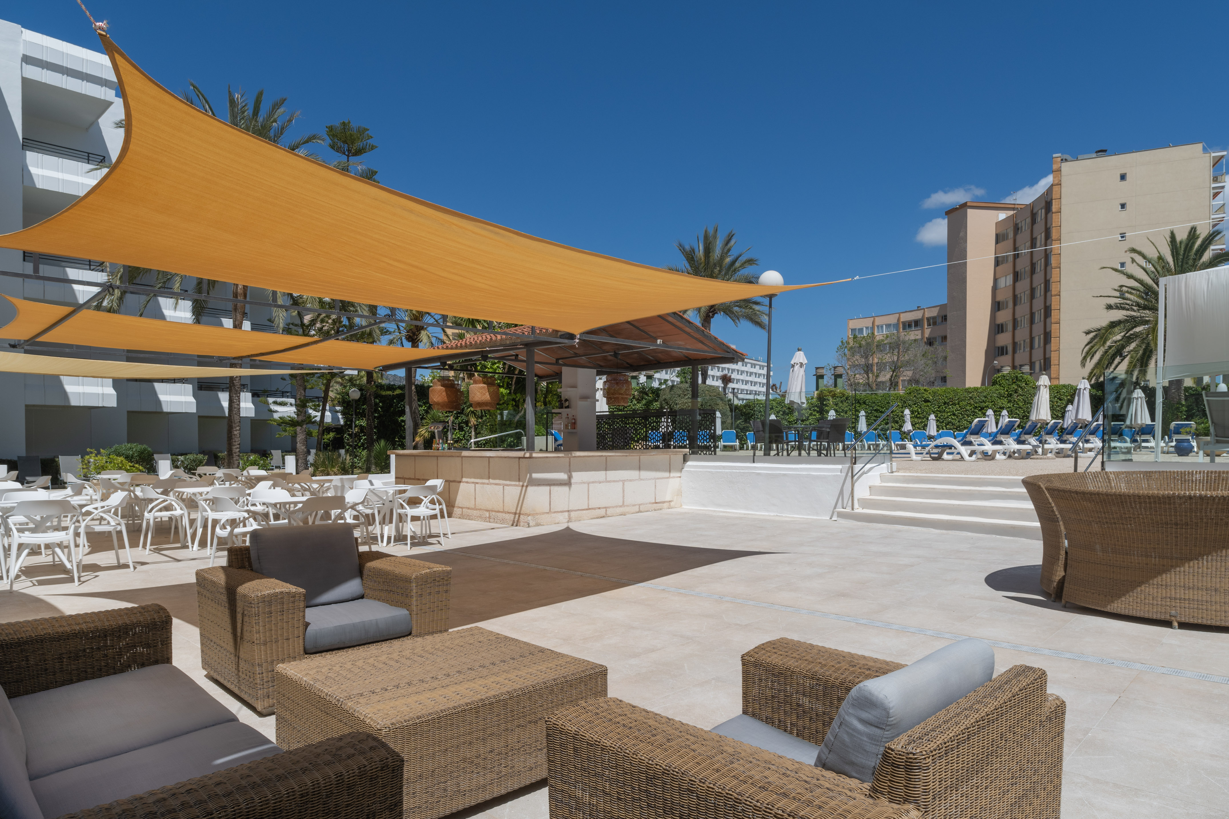 Resort outdoor lounge with orange sun shades, wicker furniture, bar, and pool deck.