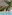 Three people relaxing by a tropical resort pool with thatched roofs and palm trees.