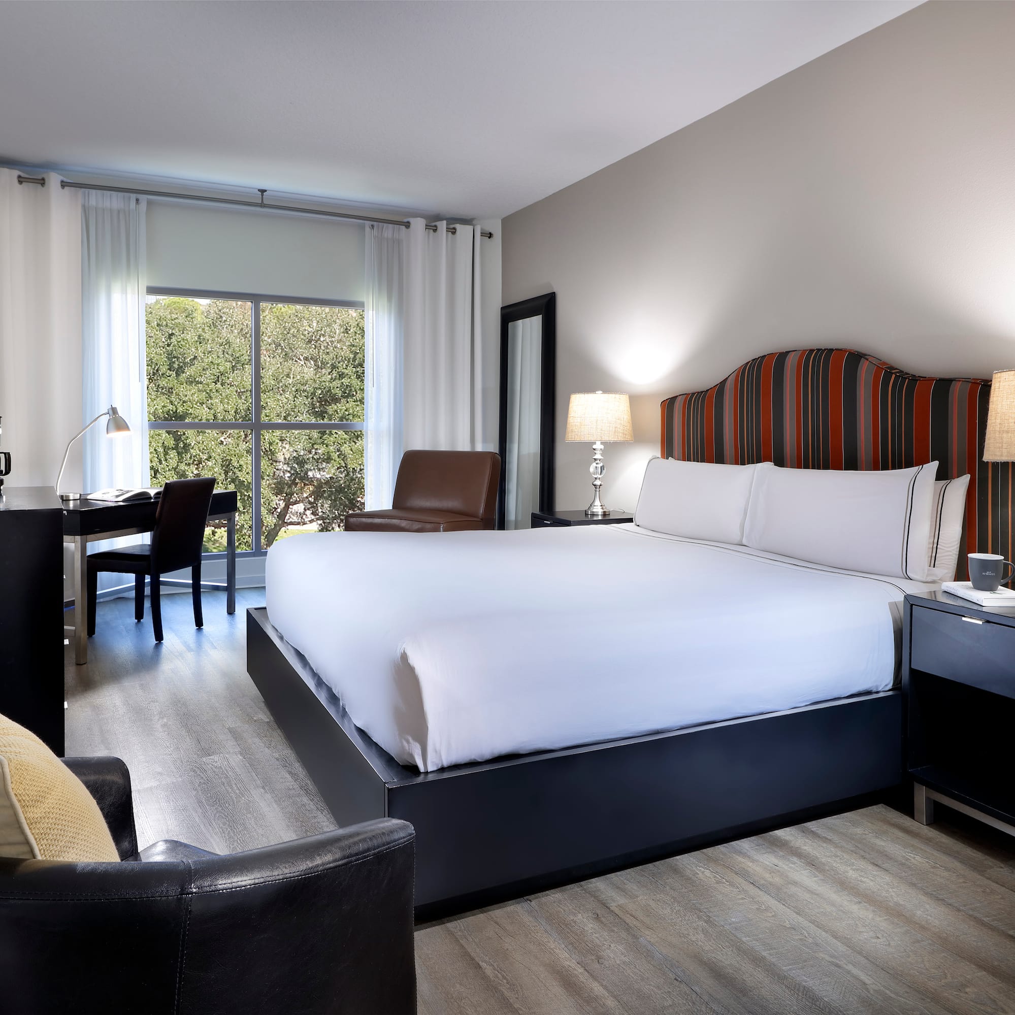 Modern hotel room with king bed, striped headboard, work desk, and window view.
