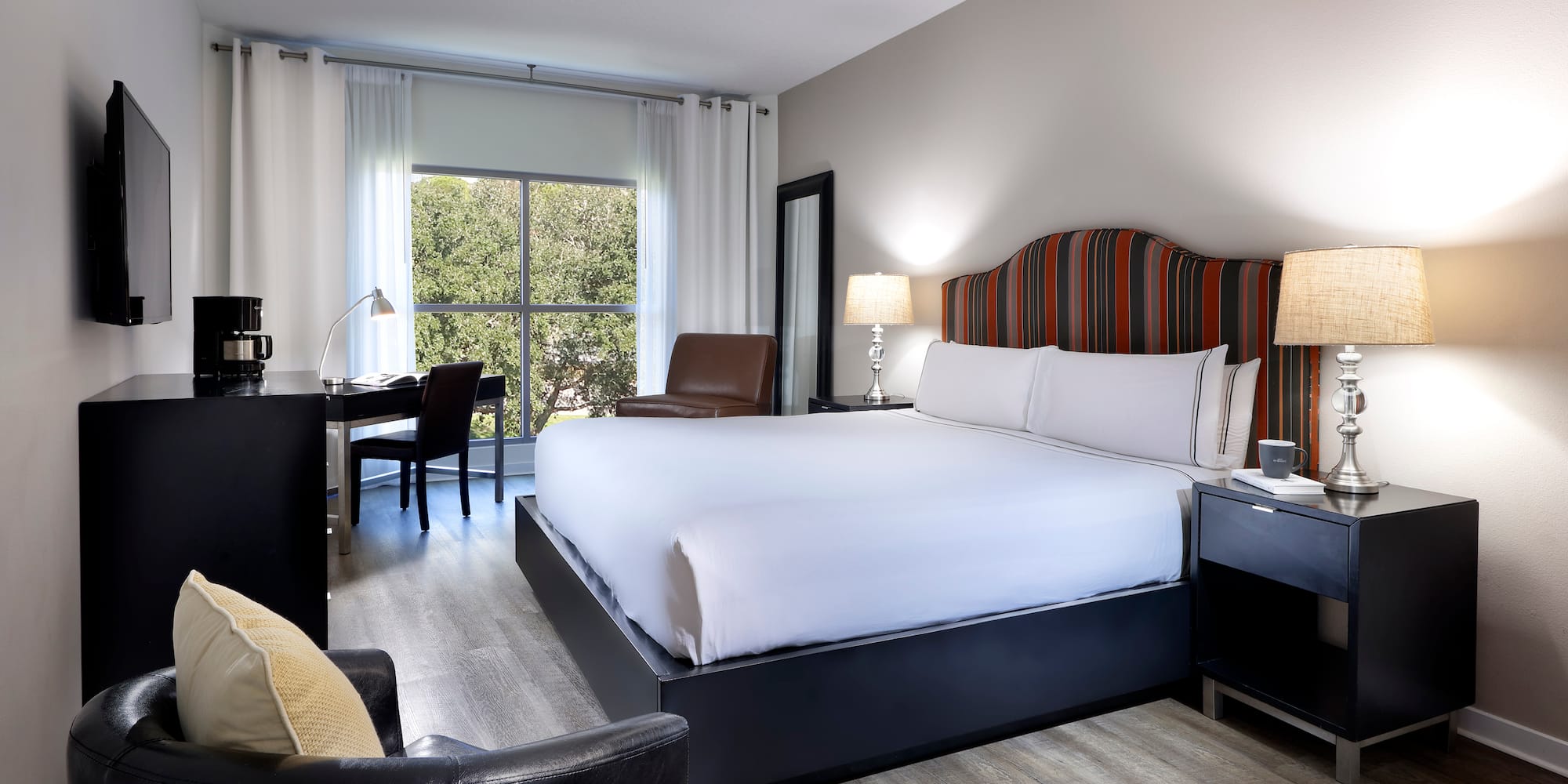 Modern hotel room with king bed, striped headboard, work desk, and window view.