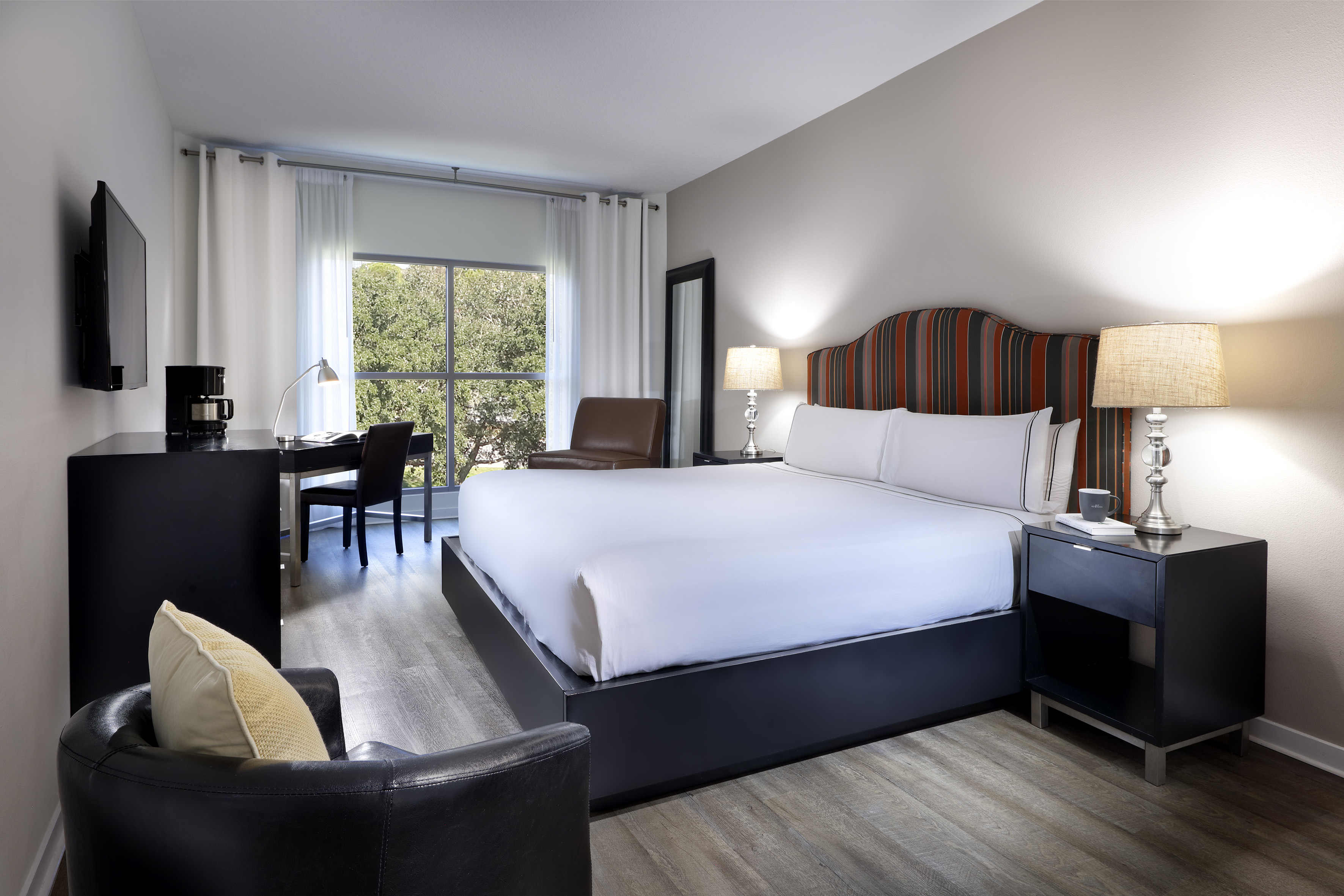 Modern hotel room with king bed, striped headboard, work desk, and window view.