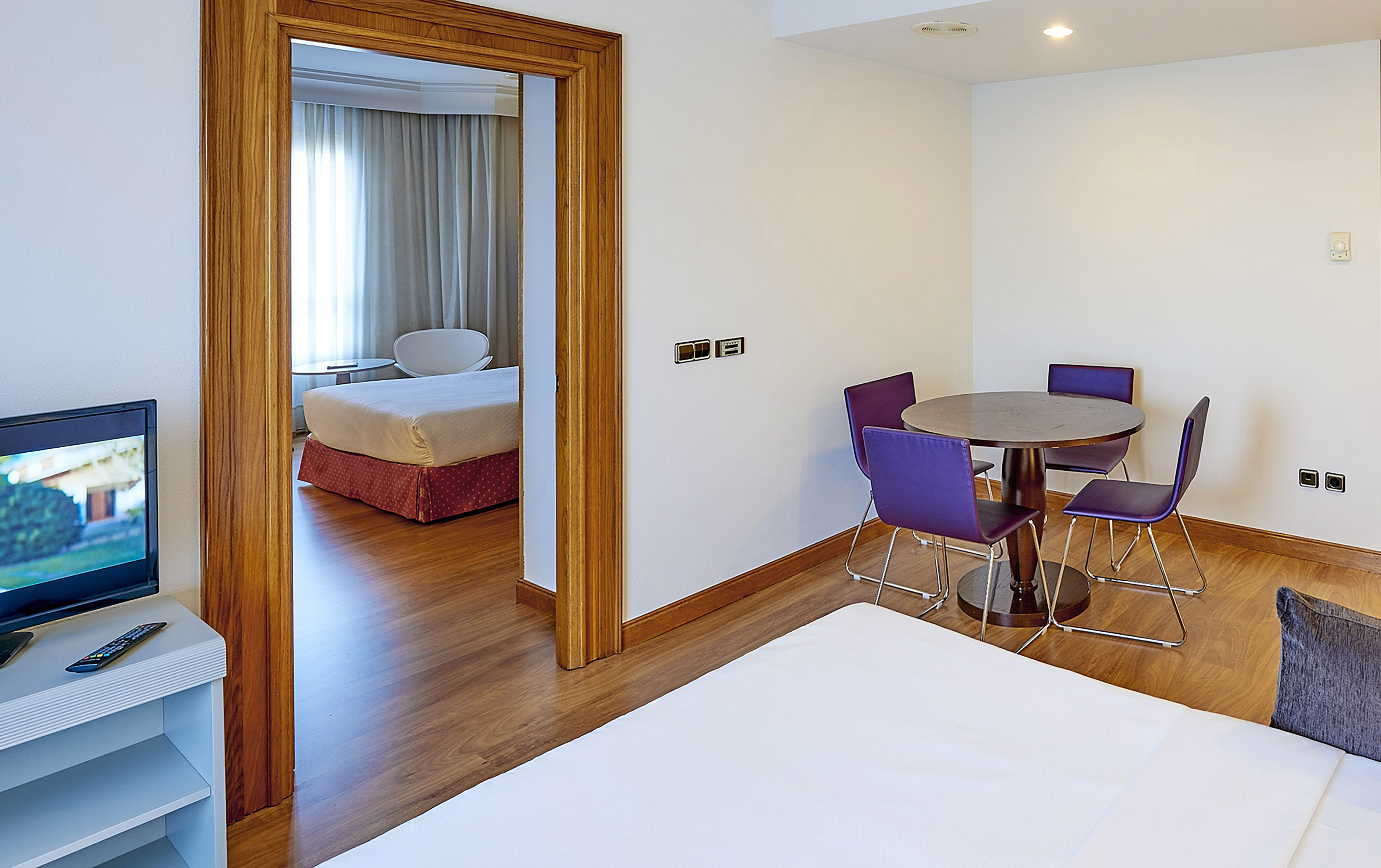 Hotel suite living area with dining table, purple chairs, and bedroom.