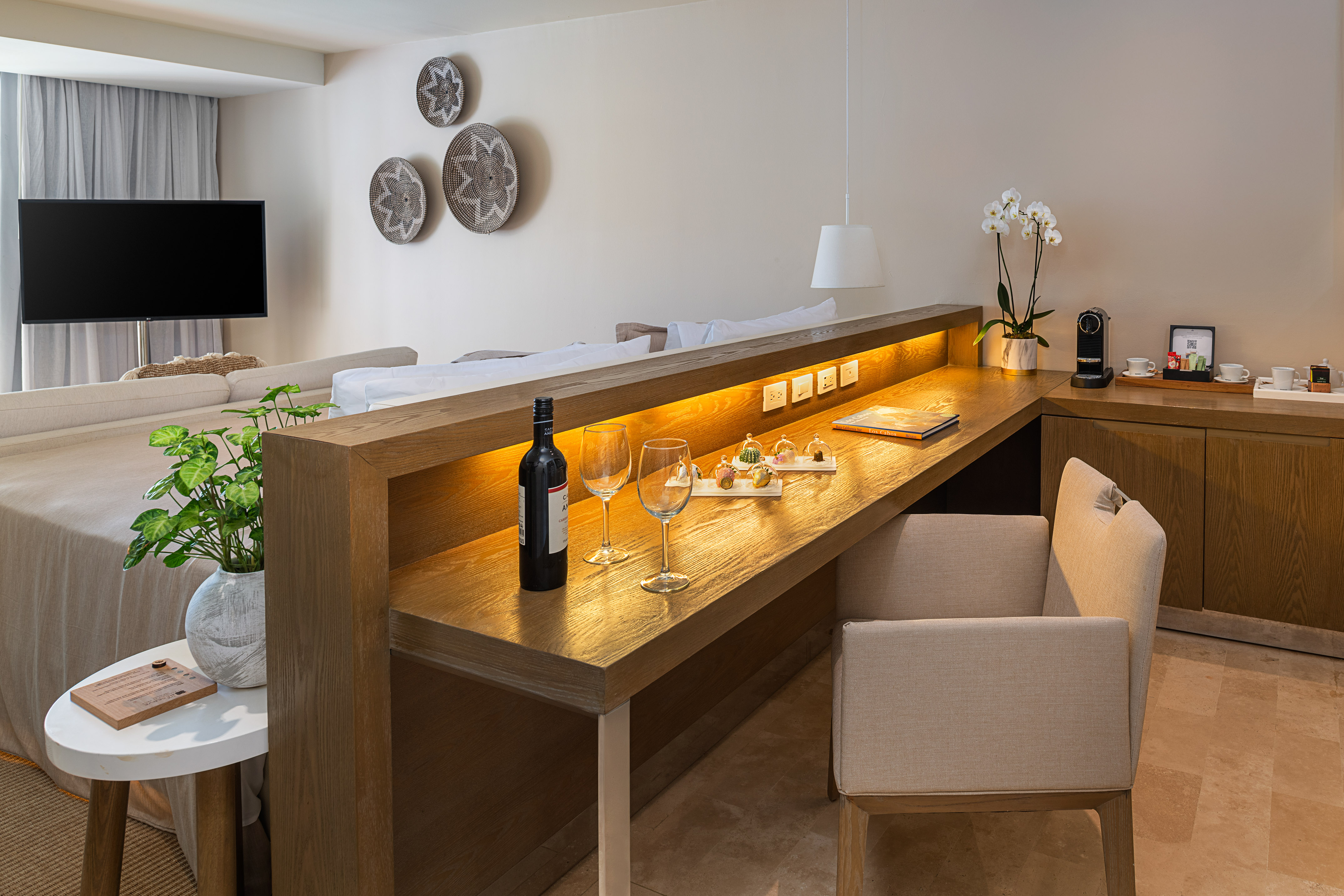 Modern hotel suite with wooden desk, wine, Nespresso, and bed.