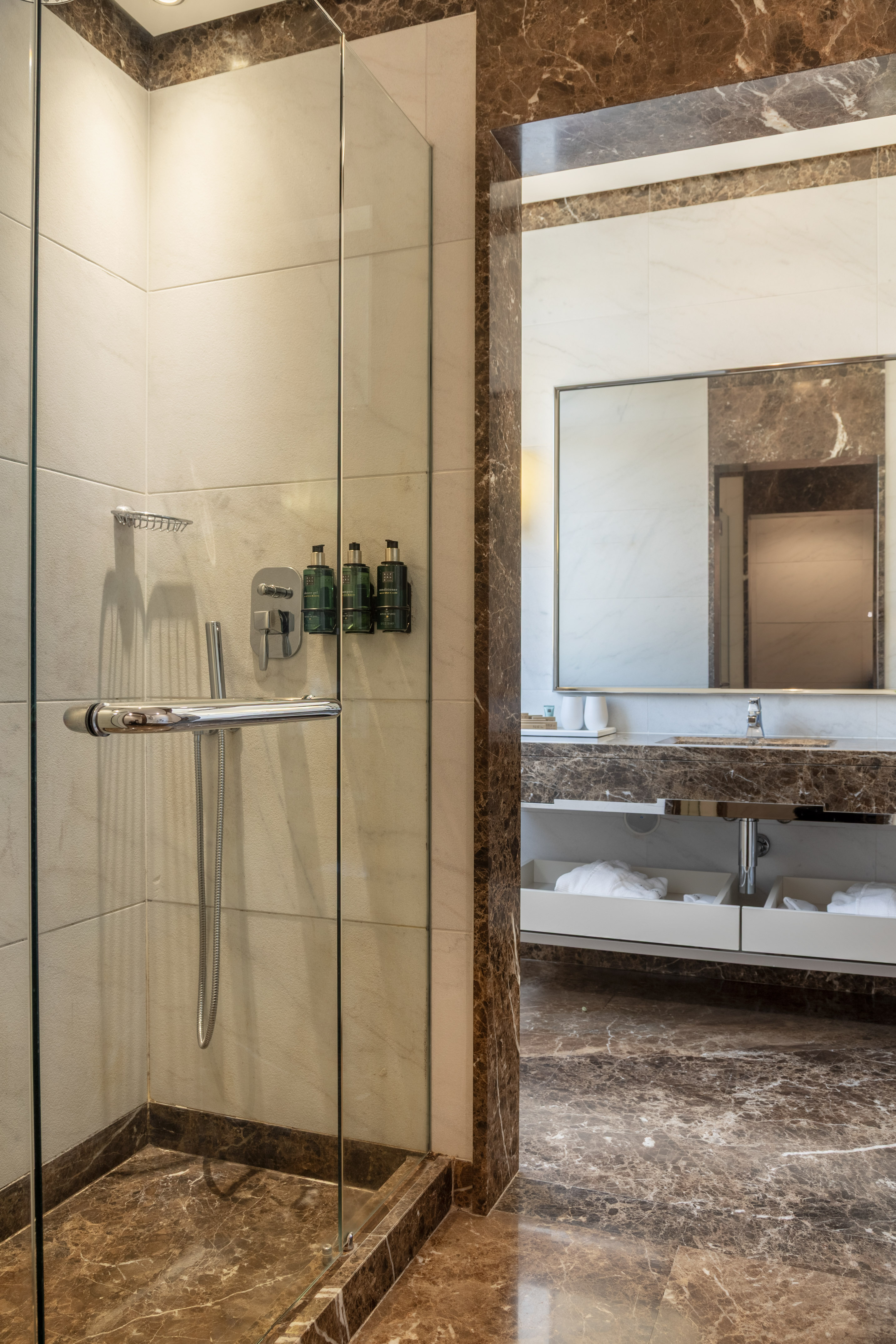 Luxury hotel bathroom with glass shower, brown marble, and vanity area.