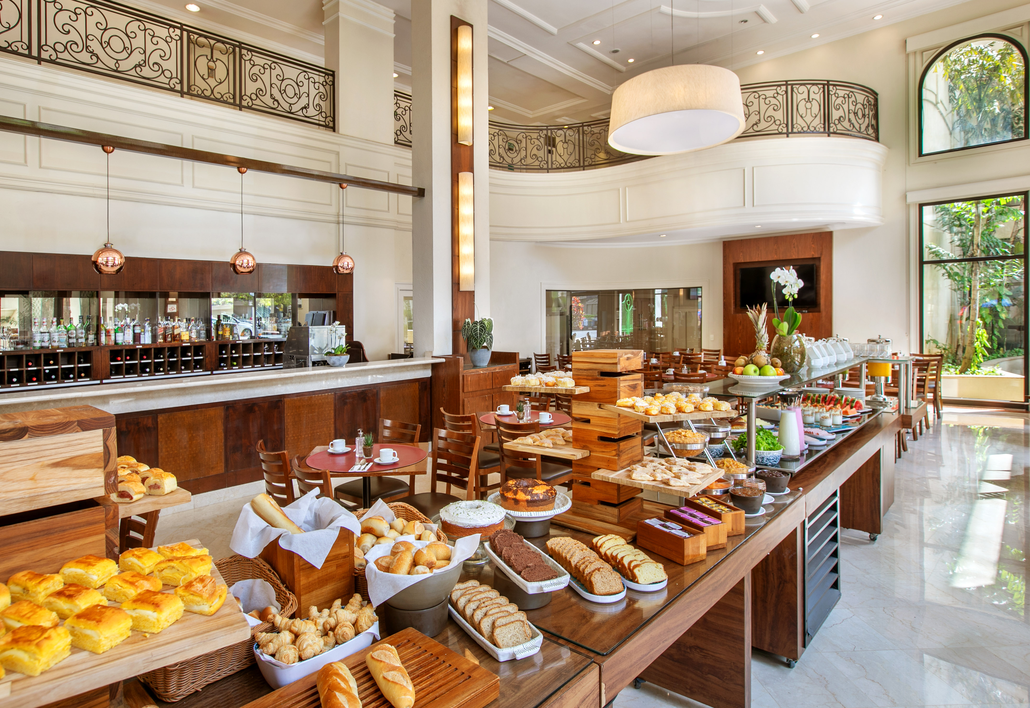 Spacious hotel buffet with pastries, bread, fresh fruits, and drinks in a grand dining room.