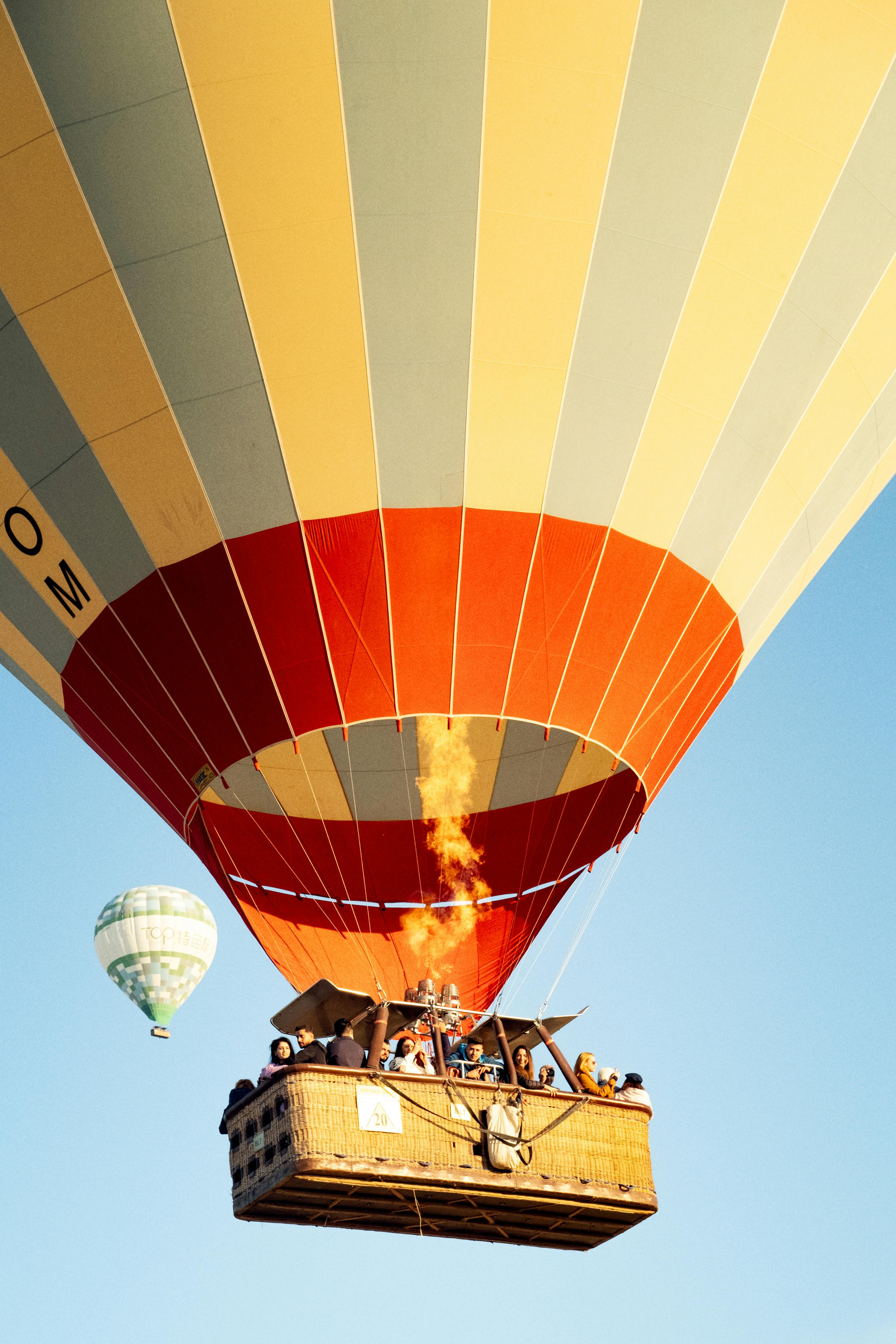 Orange hot air balloon with passengers and flame, smaller balloon in blue sky.