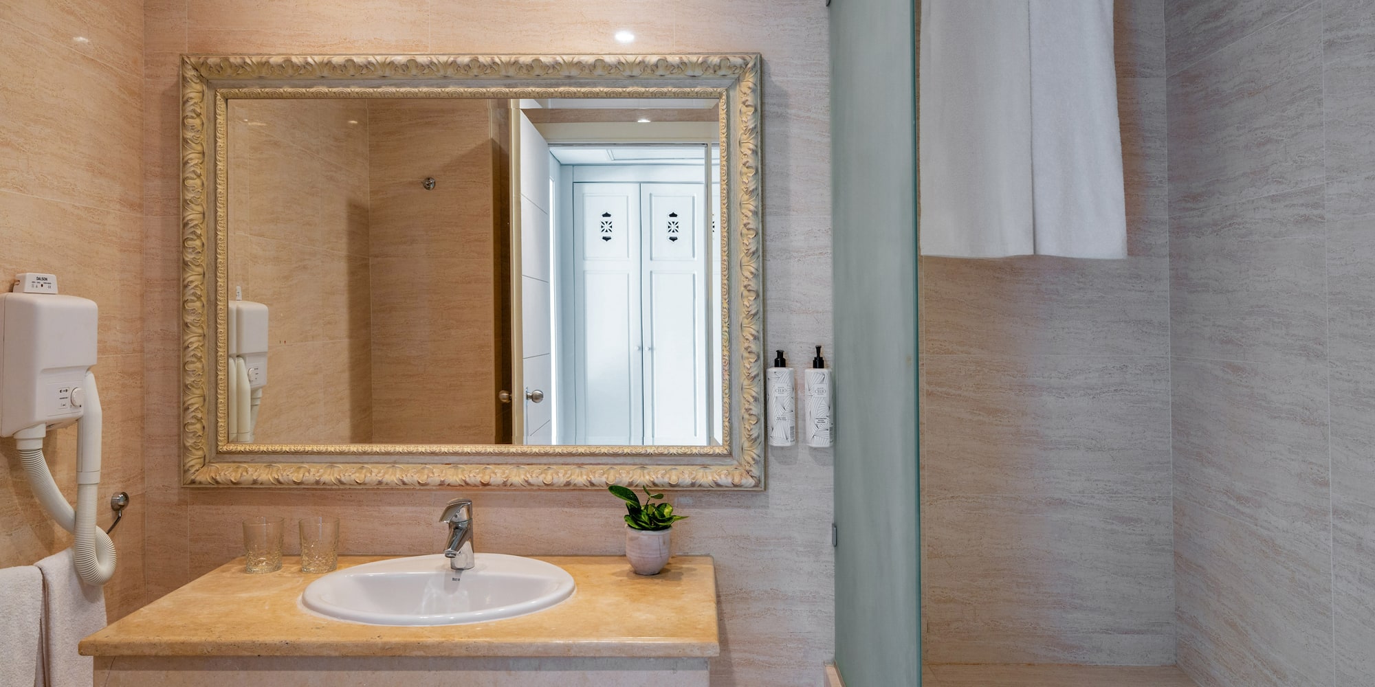 Elegant hotel bathroom with vanity, ornate mirror, sink, and tiled shower.