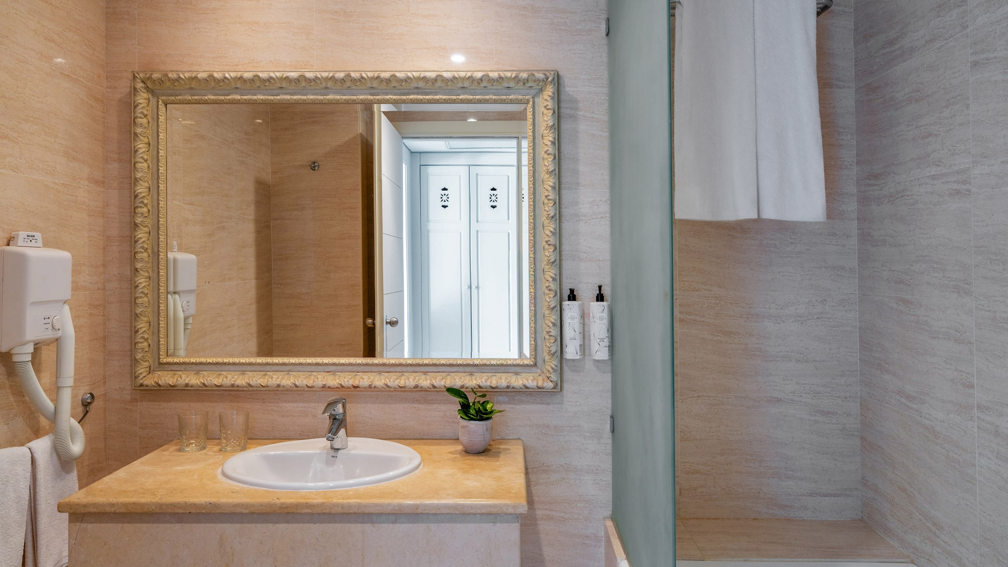 Elegant hotel bathroom with vanity, ornate mirror, sink, and tiled shower.