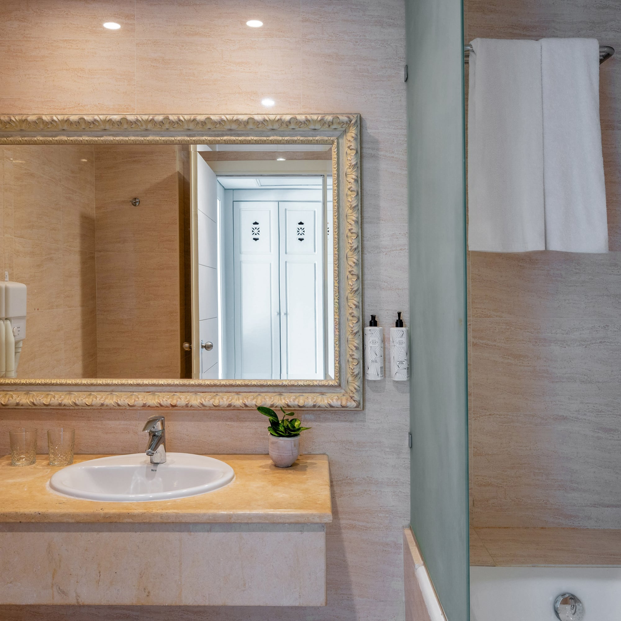 Elegant hotel bathroom with vanity, ornate mirror, sink, and tiled shower.