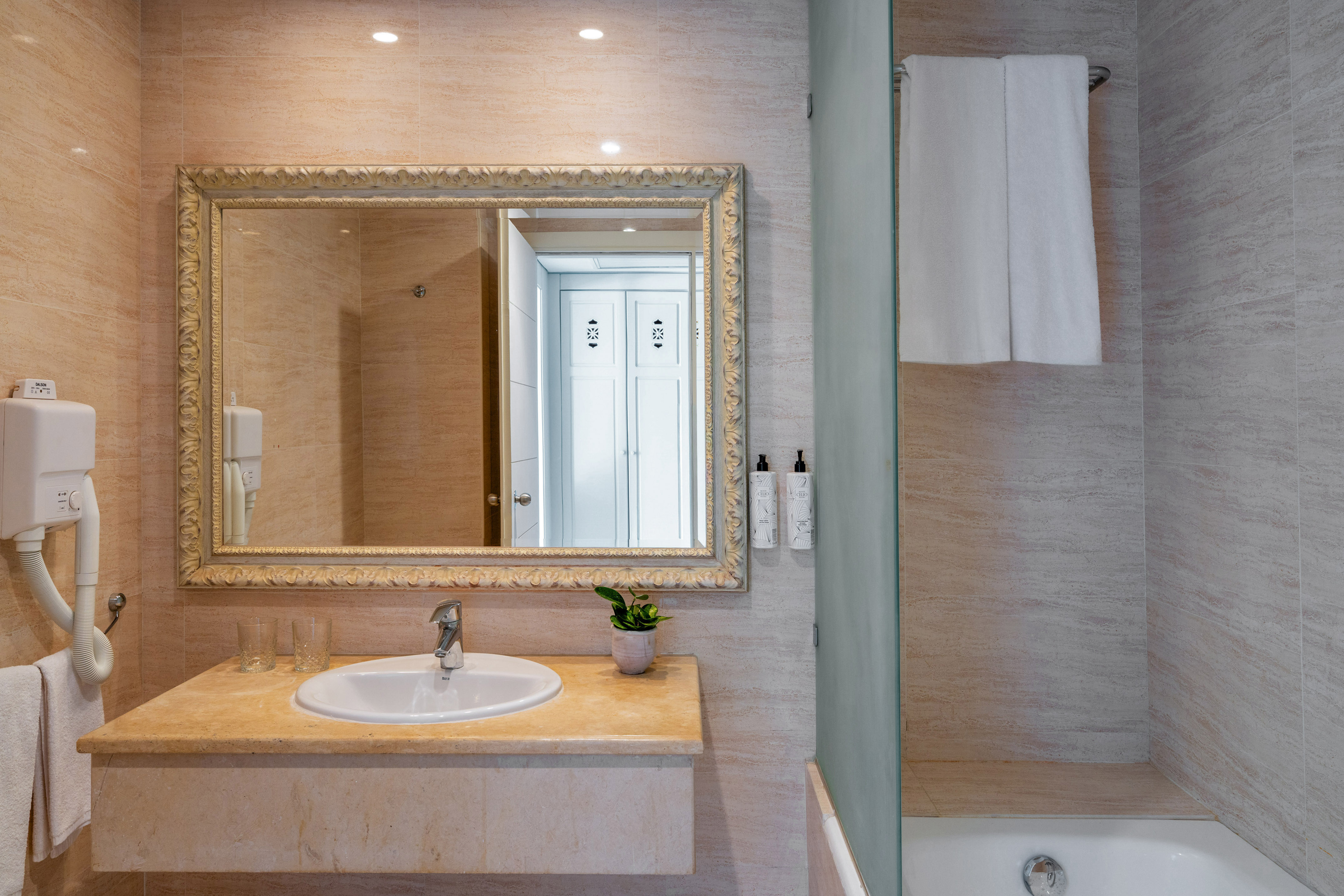 Elegant hotel bathroom with vanity, ornate mirror, sink, and tiled shower.