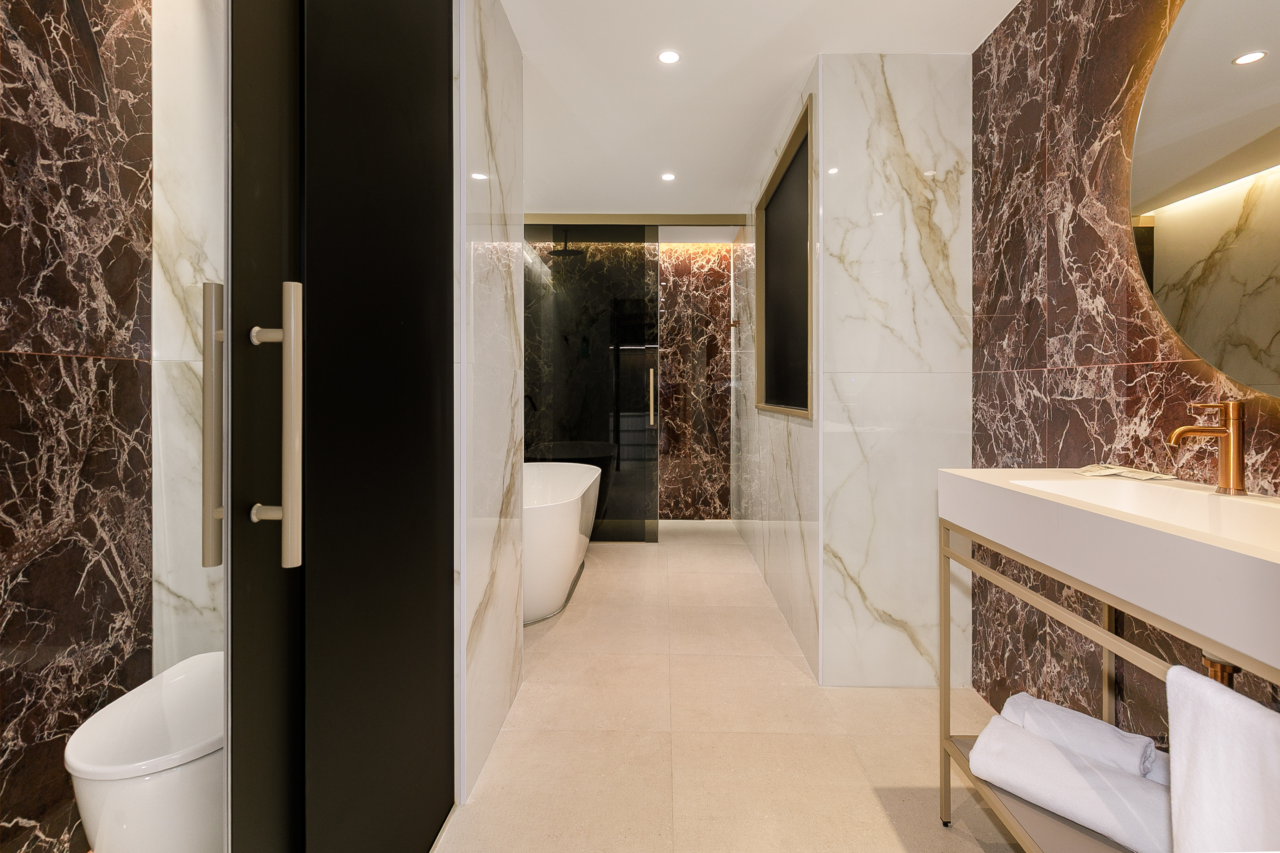 Elegant bathroom with dark marble walls, freestanding tub, gold faucet, and vanity.