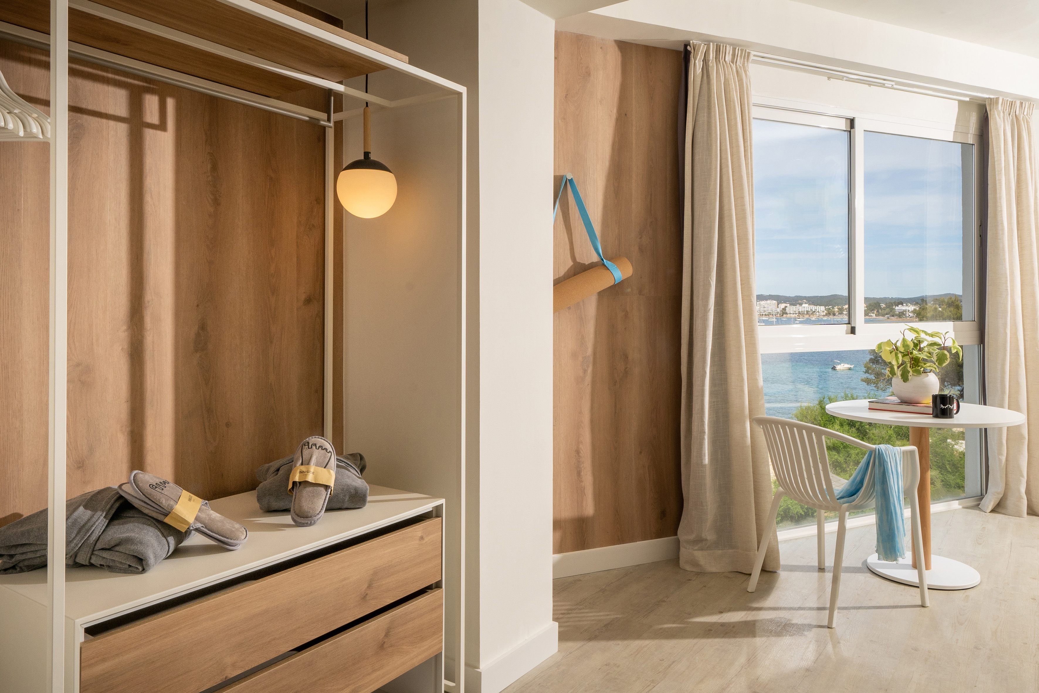 Bright hotel room with sea view, built-in wardrobe, slippers, and yoga mat.
