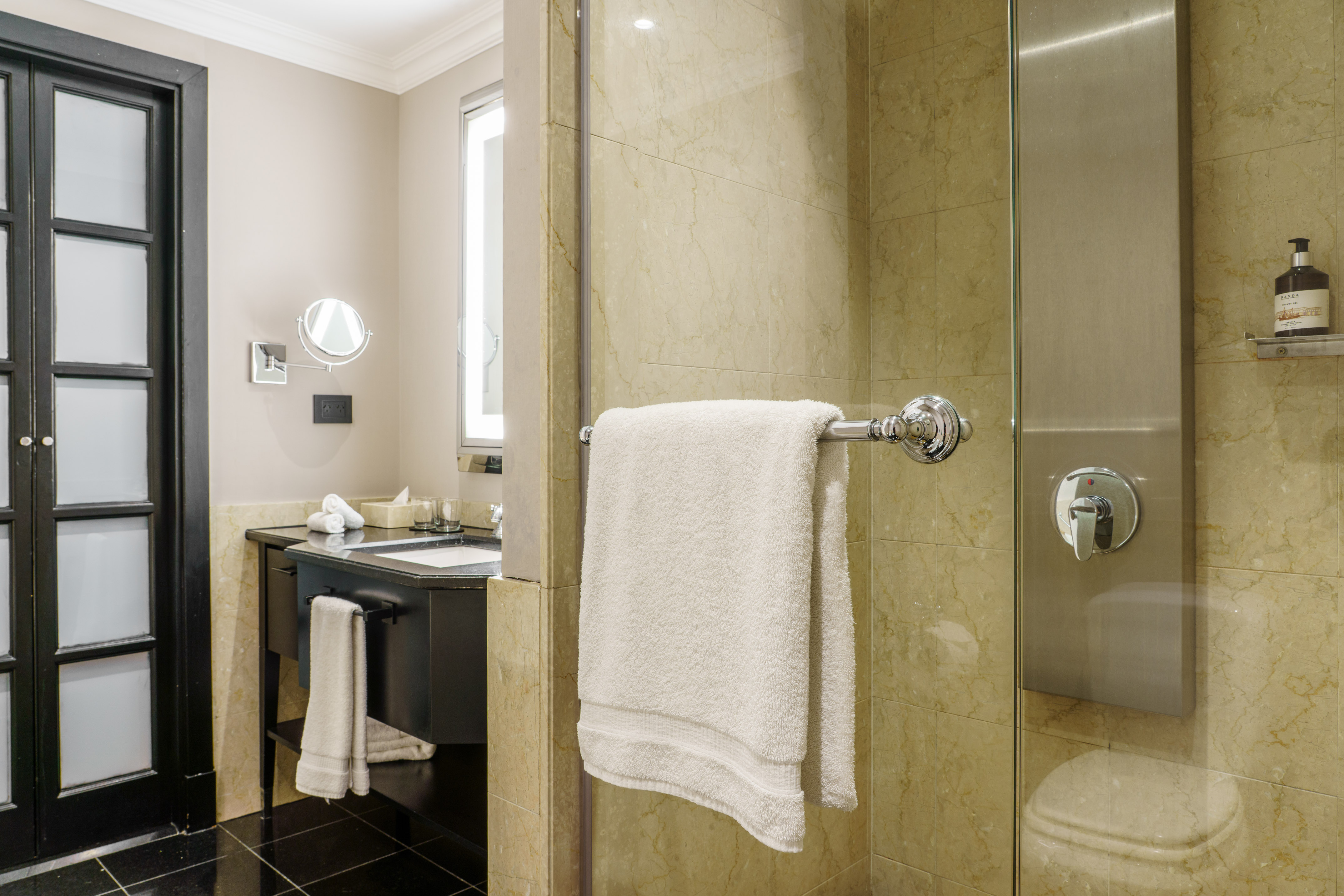 Contemporary bathroom with black vanity, lighted mirror, white towels, and marble shower.