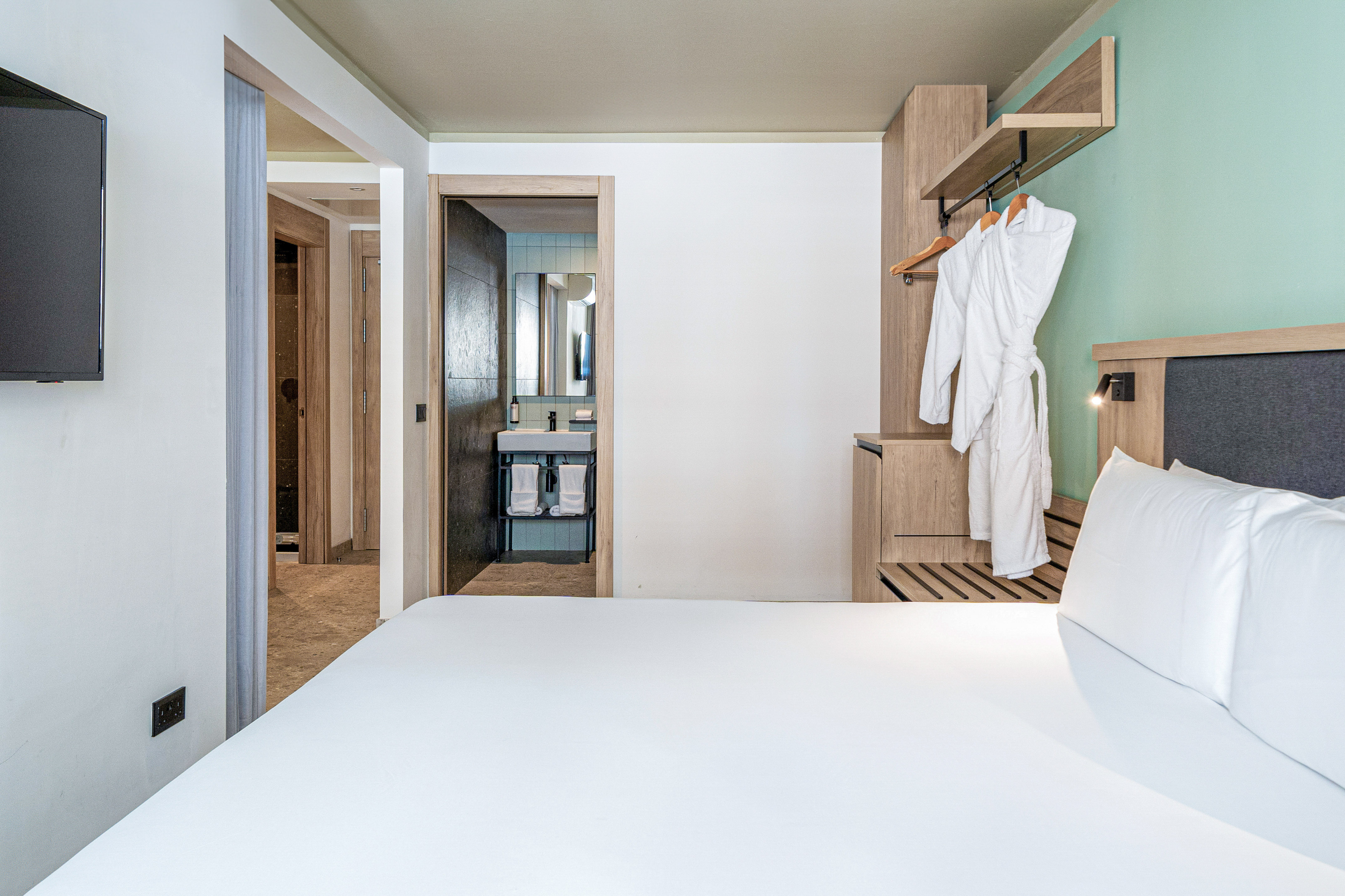 Modern hotel room with bed, open wardrobe, and connected bathroom.