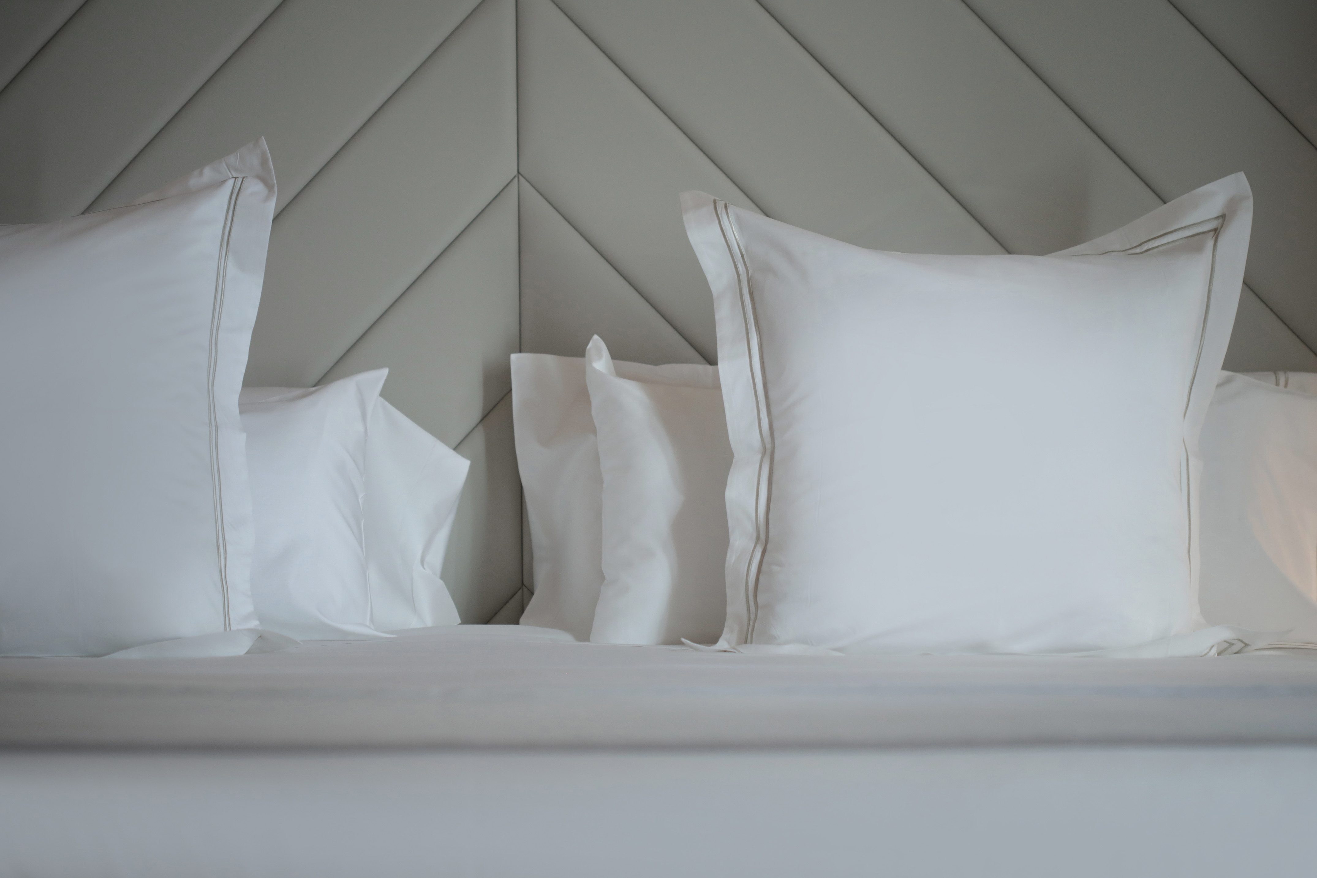 Neatly made hotel bed with crisp white pillows and geometric headboard.