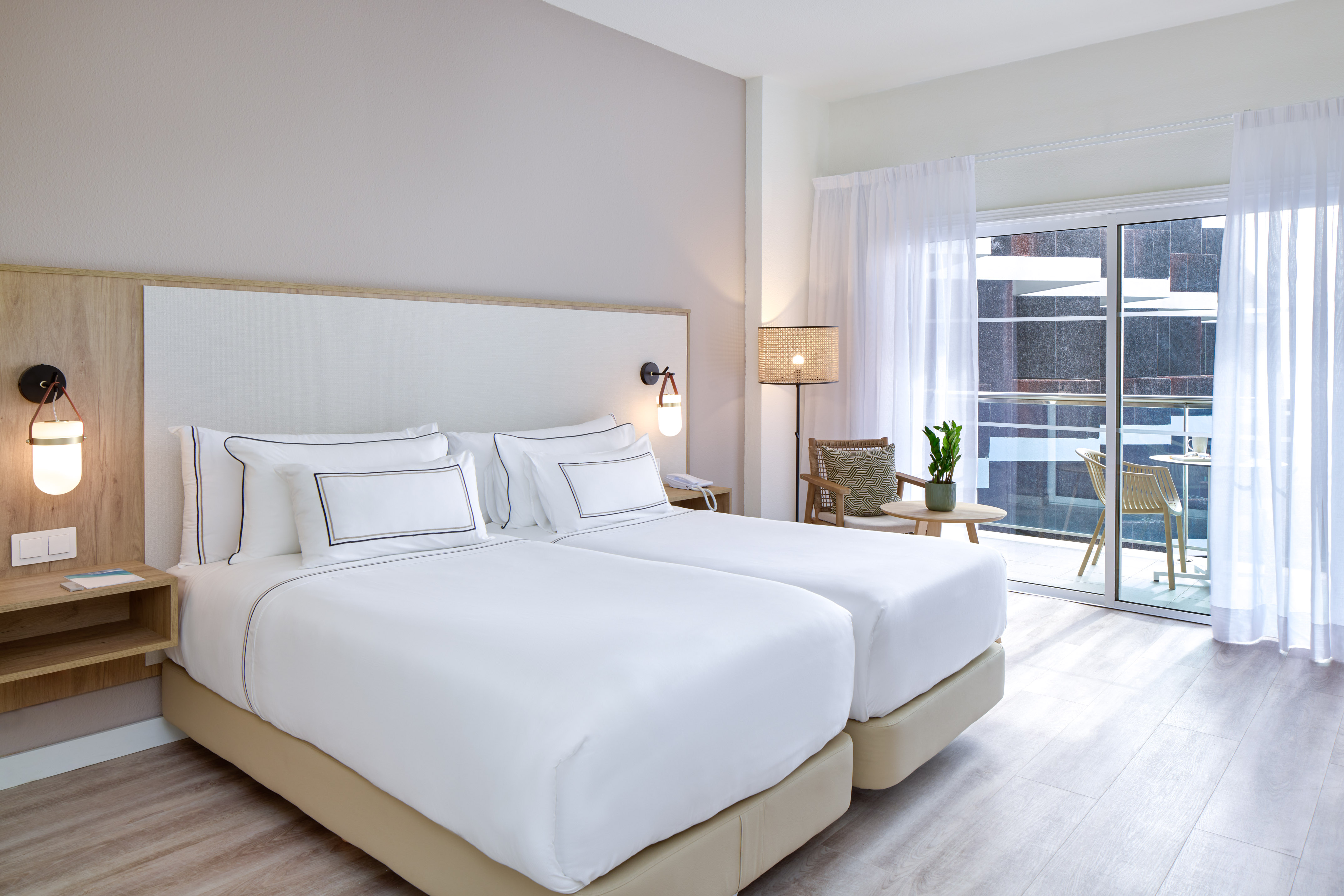 Modern hotel room with twin beds, balcony access, and minimalist decor.