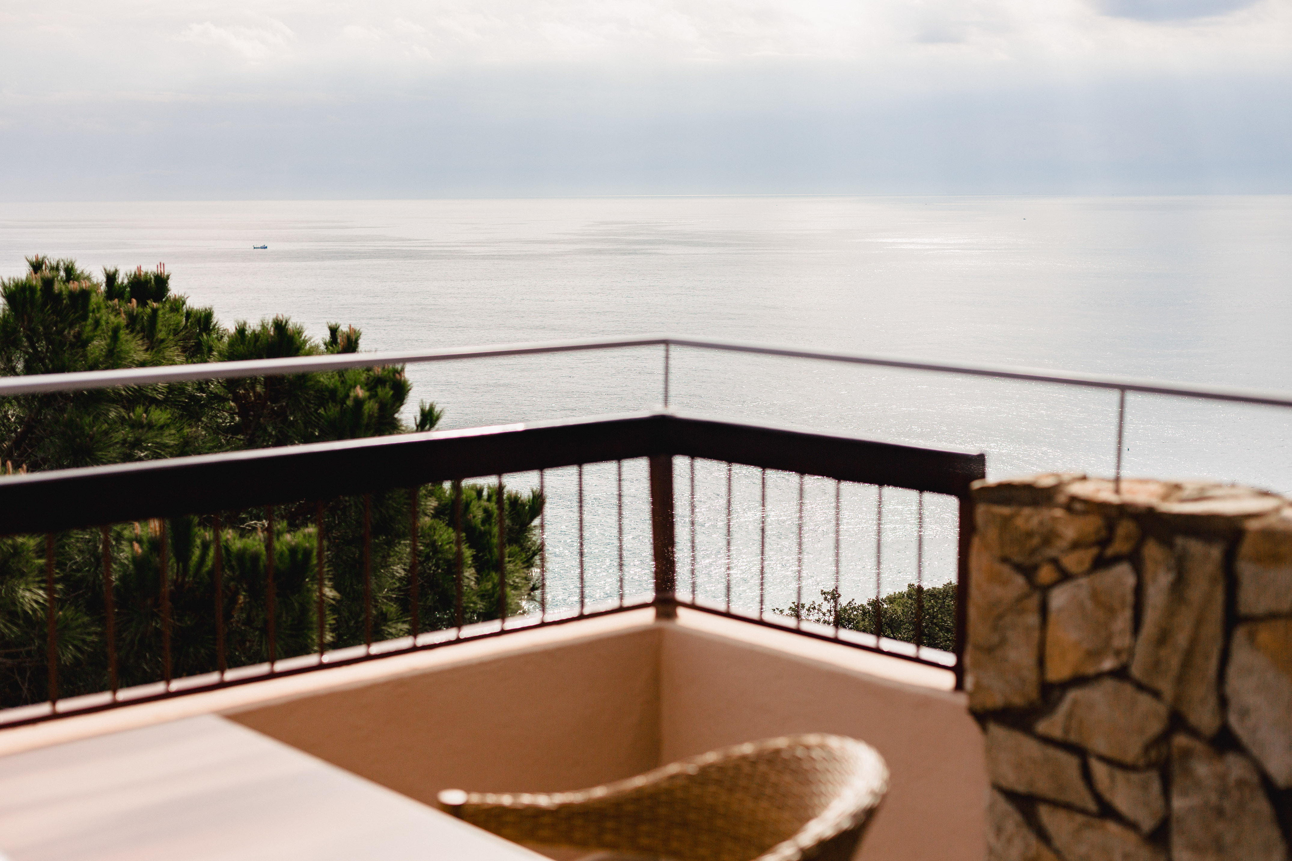 Balcony sea view with metal railing, green trees, and calm ocean.