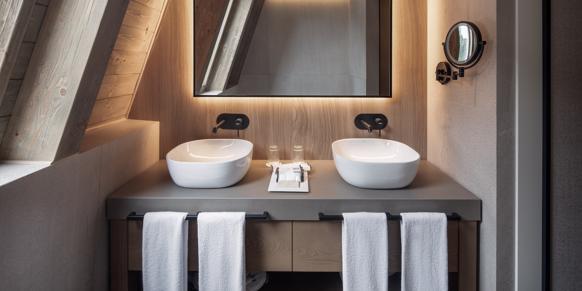 Double vanity with vessel sinks, backlit mirror, and sloped wood ceiling.