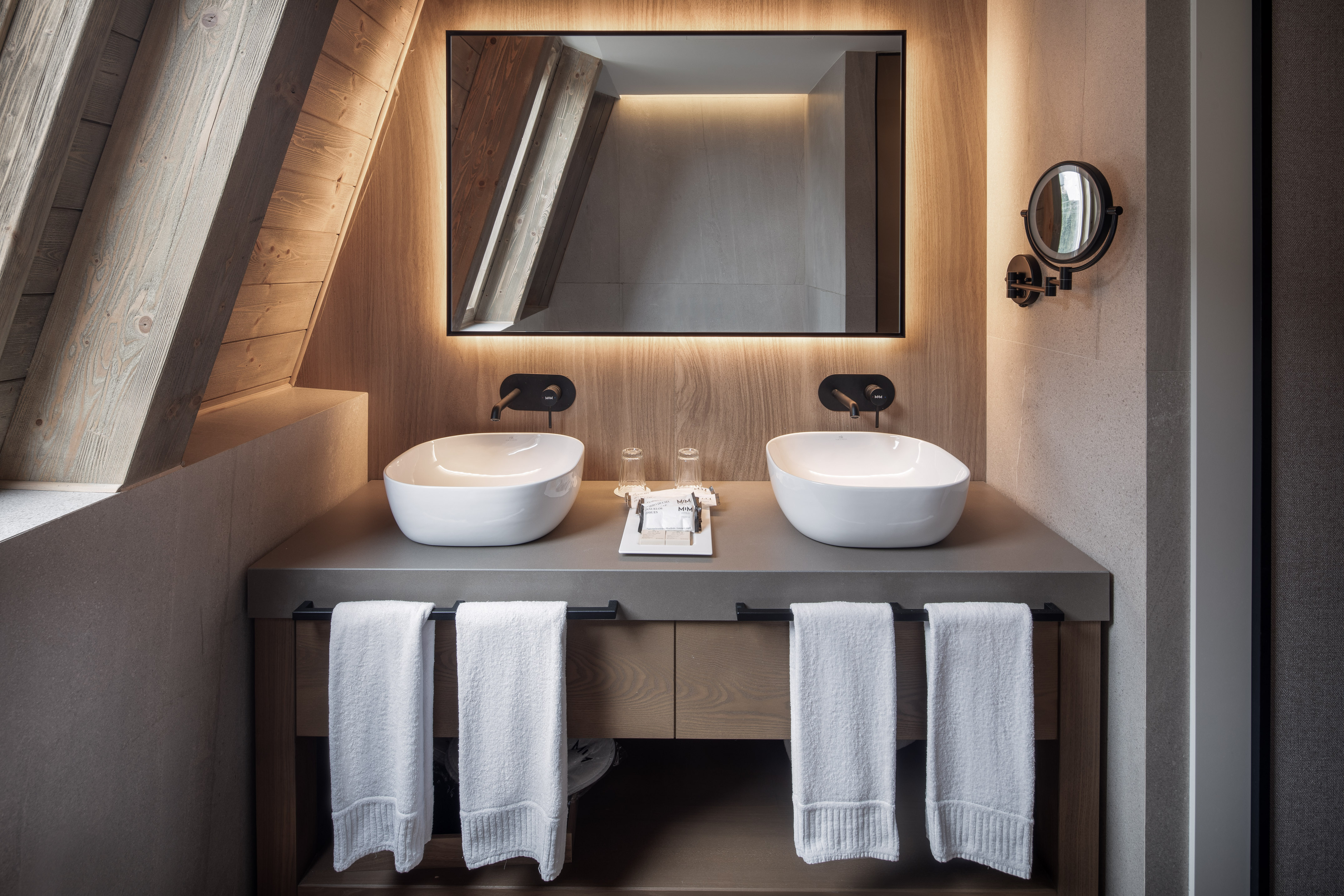 Double vanity with vessel sinks, backlit mirror, and sloped wood ceiling.
