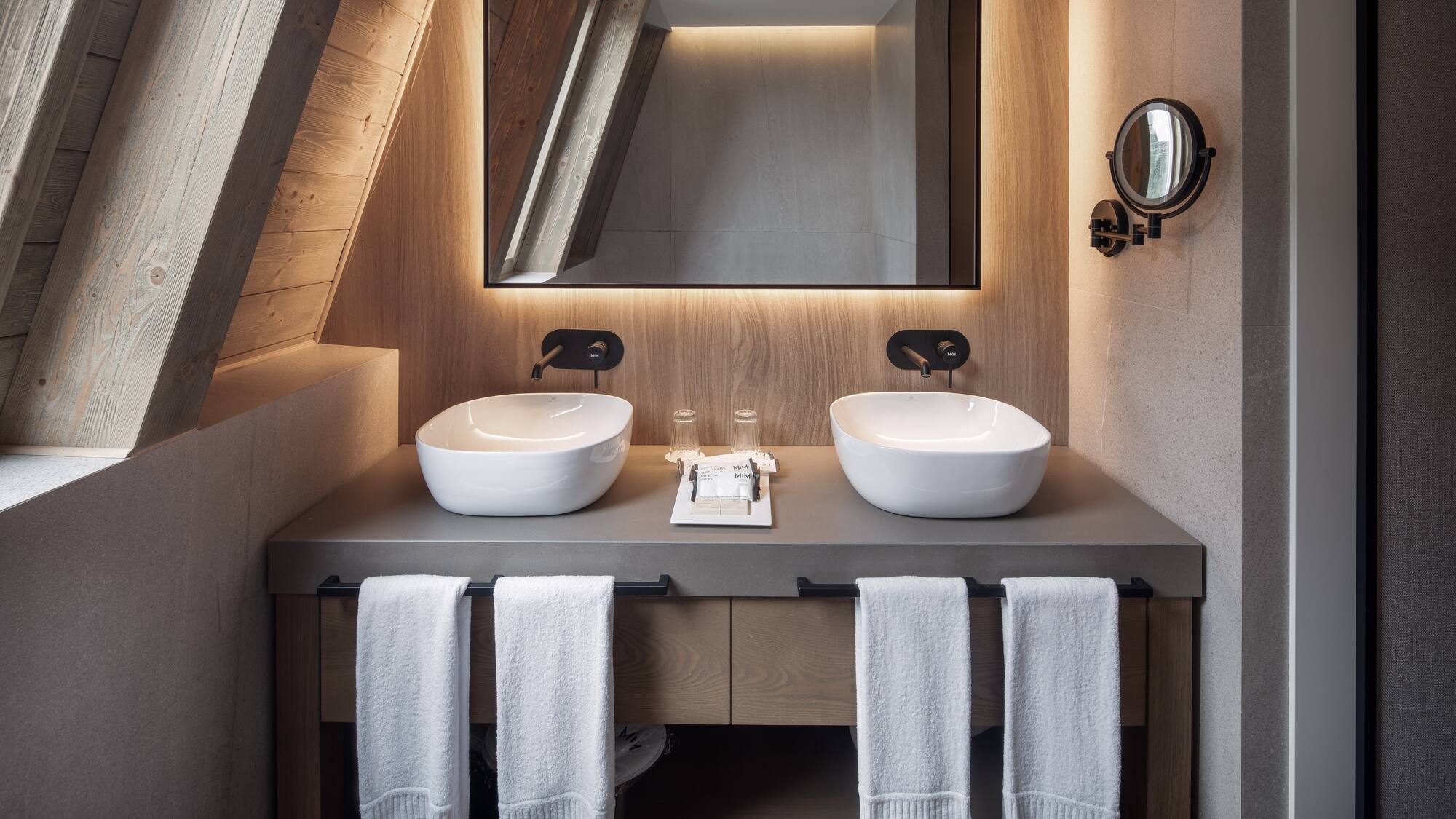 Double vanity with vessel sinks, backlit mirror, and sloped wood ceiling.