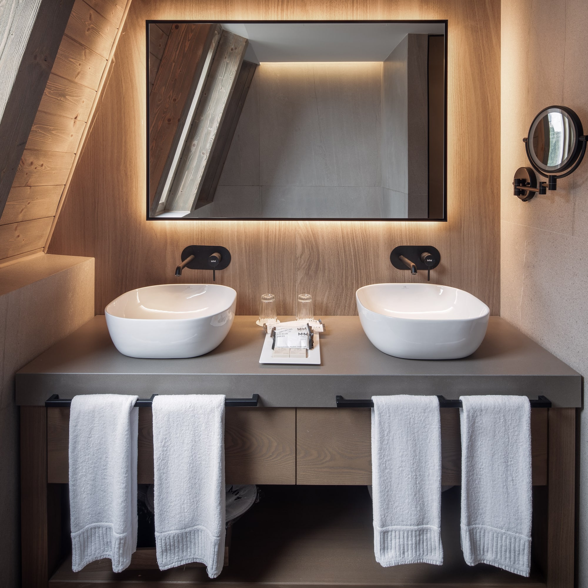 Double vanity with vessel sinks, backlit mirror, and sloped wood ceiling.