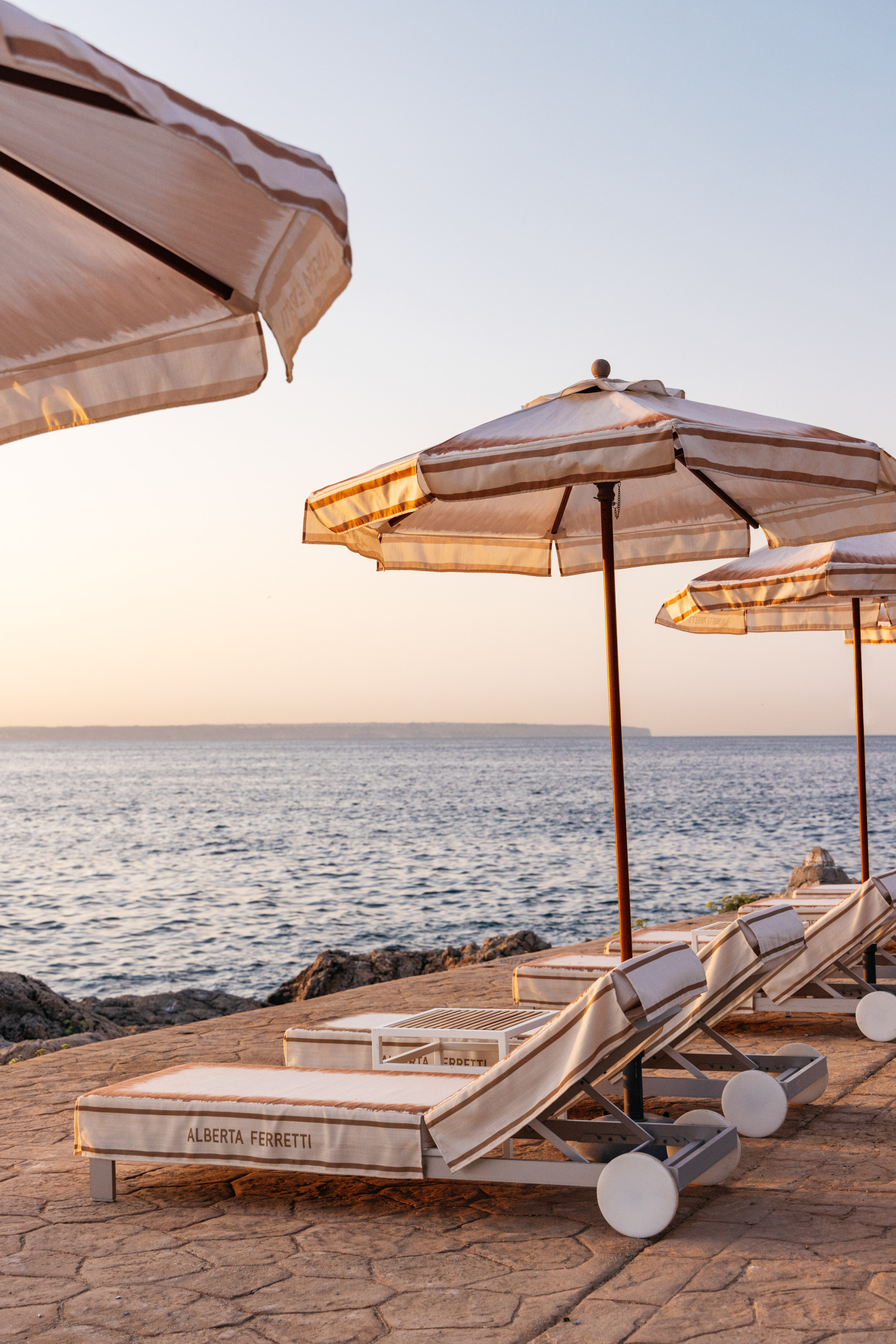 Alberta Ferretti striped lounge chairs and umbrellas by the sea at sunset.