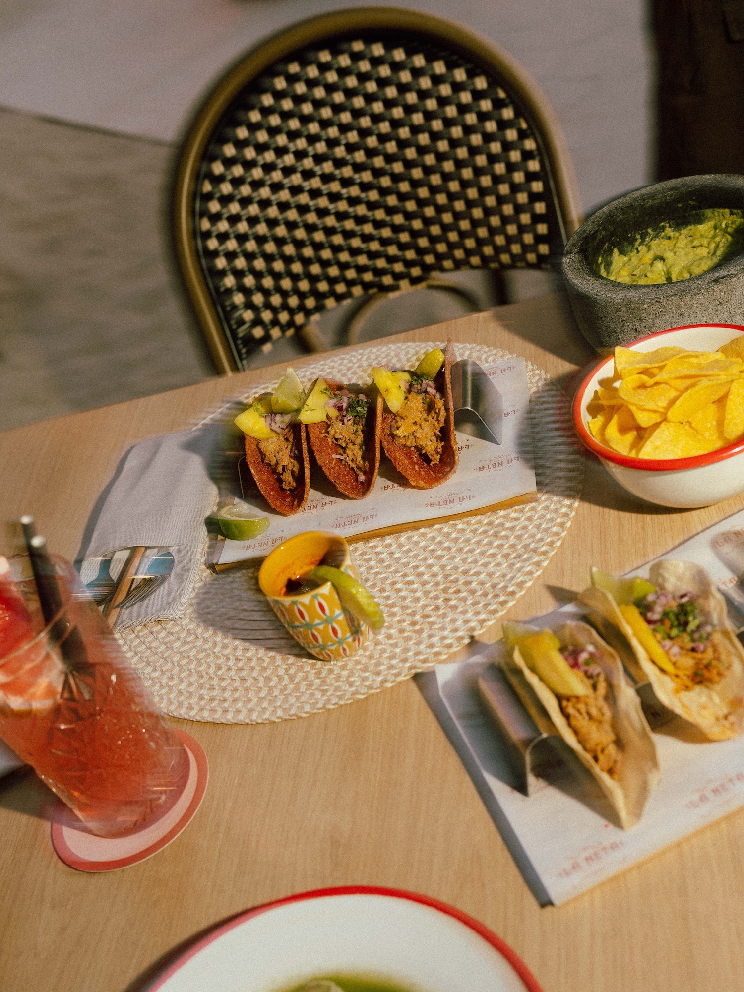 Vibrant tacos, guacamole, chips, and refreshing drinks on a wooden table.