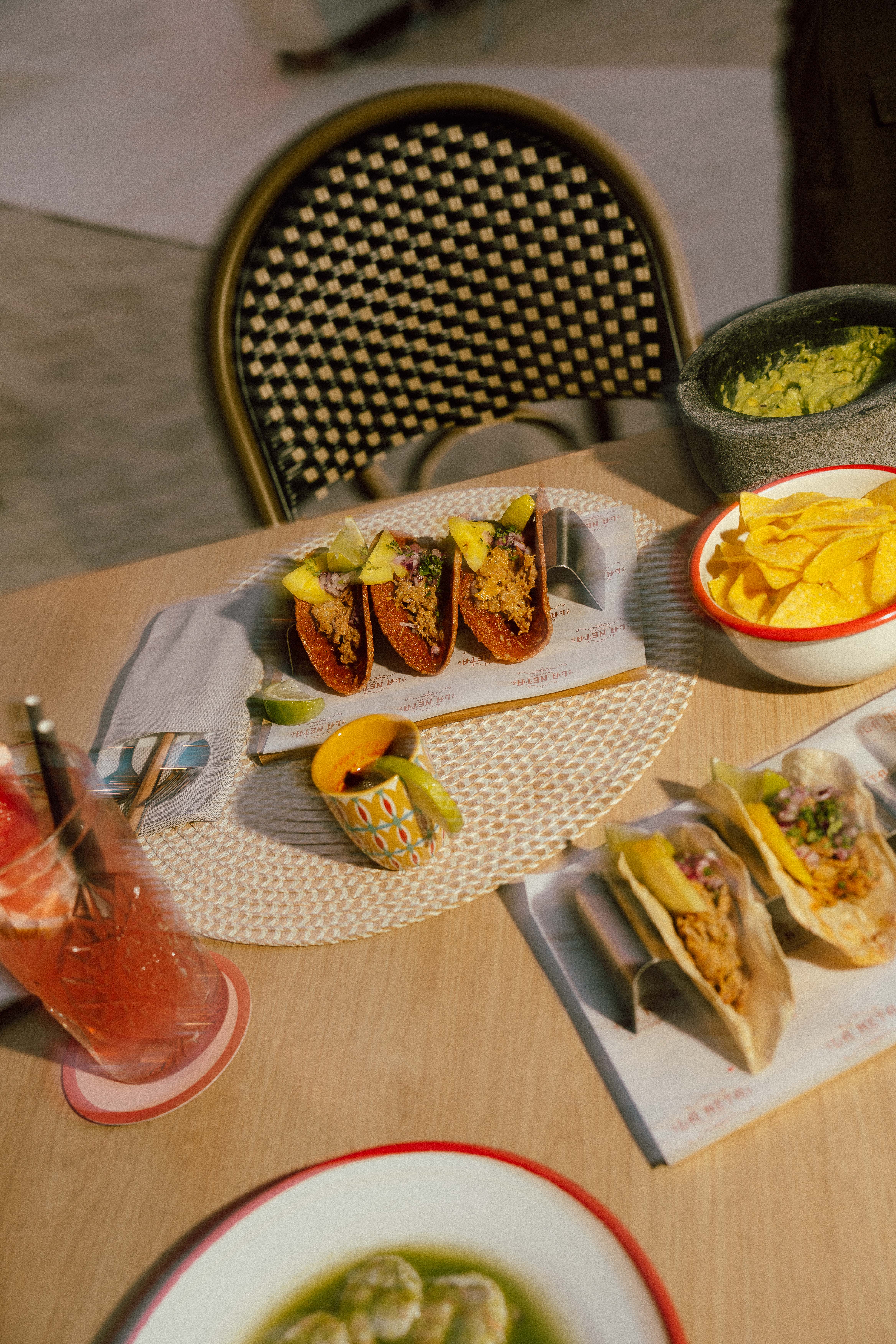 Vibrant tacos, guacamole, chips, and refreshing drinks on a wooden table.