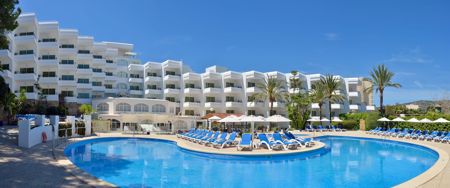 a pool with chairs and umbrellas in front of a hotel