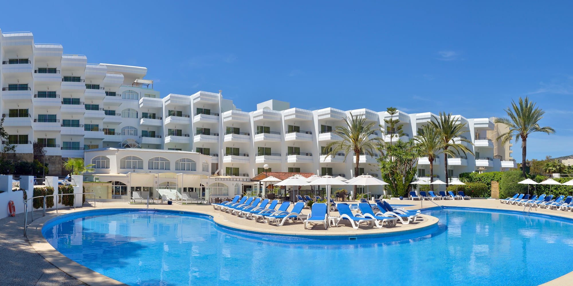 a pool with chairs and umbrellas in front of a hotel