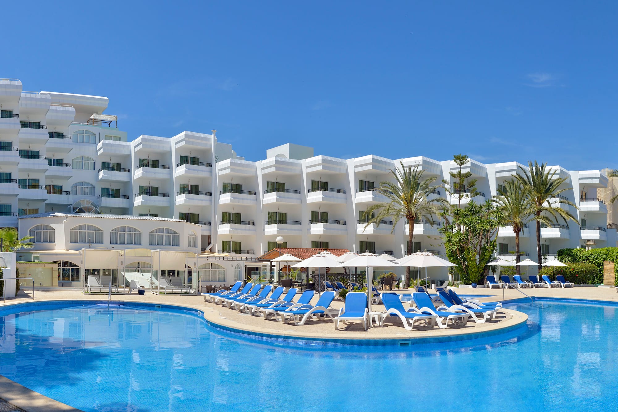a pool with chairs and umbrellas in front of a hotel