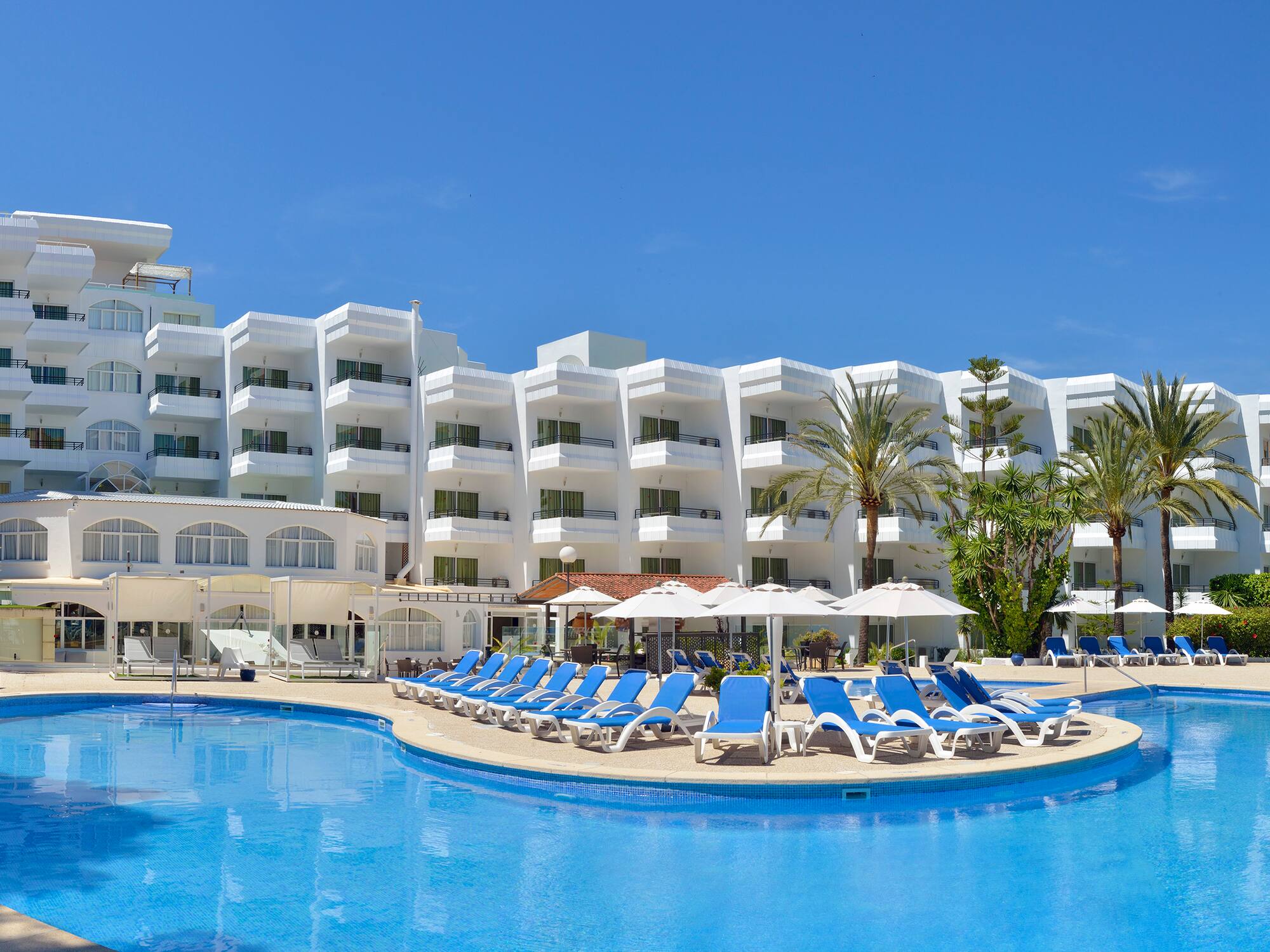 a pool with chairs and umbrellas in front of a hotel