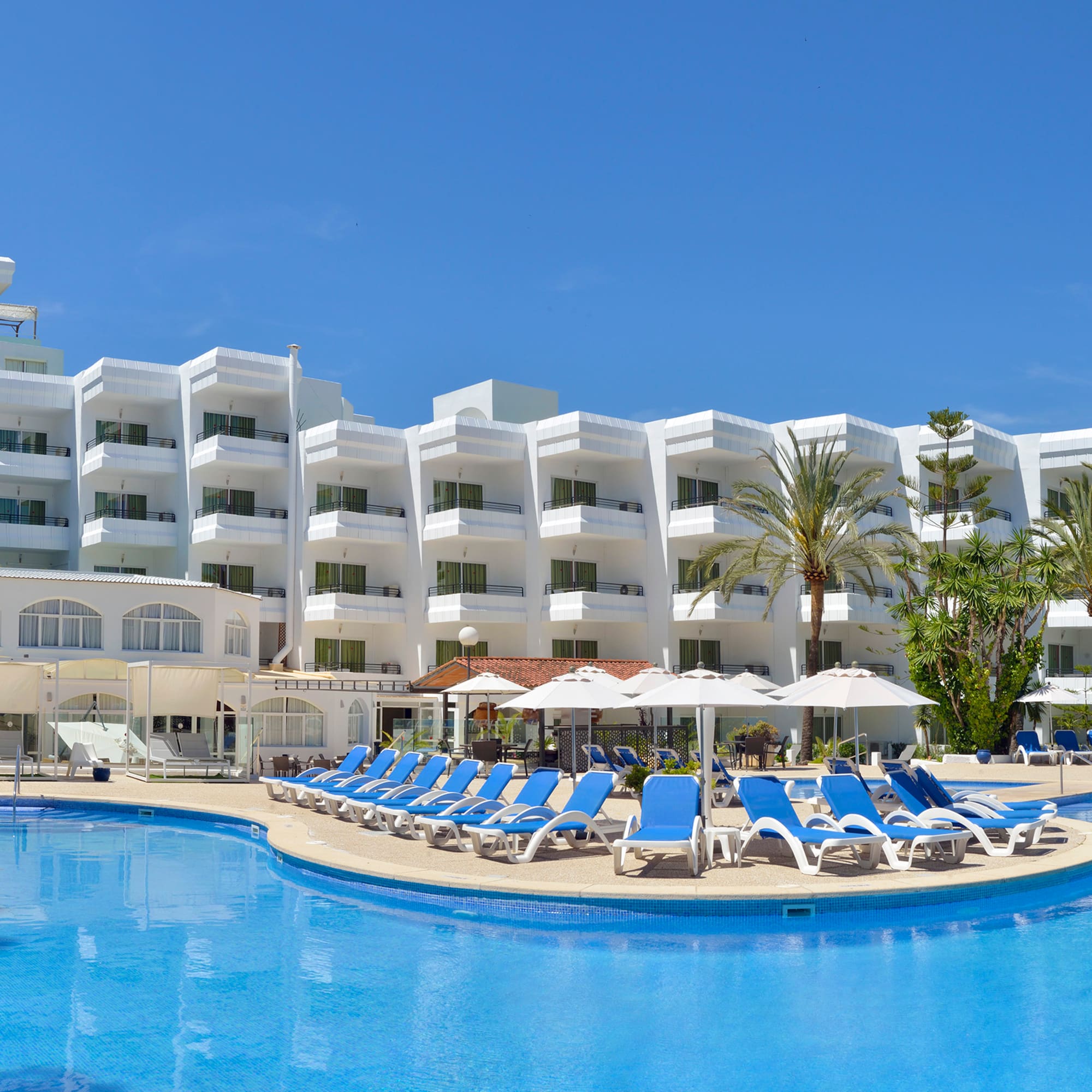 a pool with chairs and umbrellas in front of a hotel