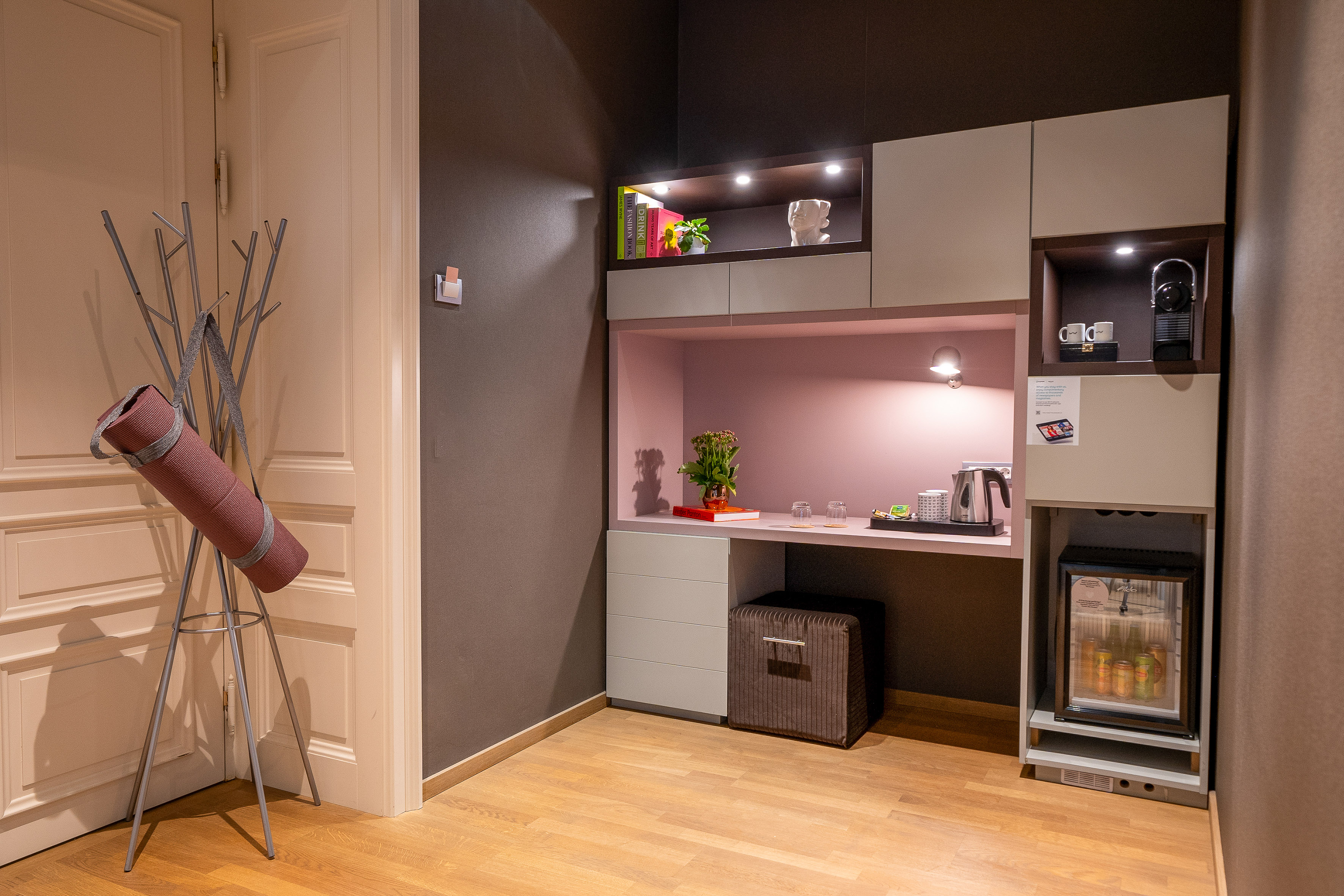 Modern hotel room with coffee machine, mini-bar, desk, and yoga mat.