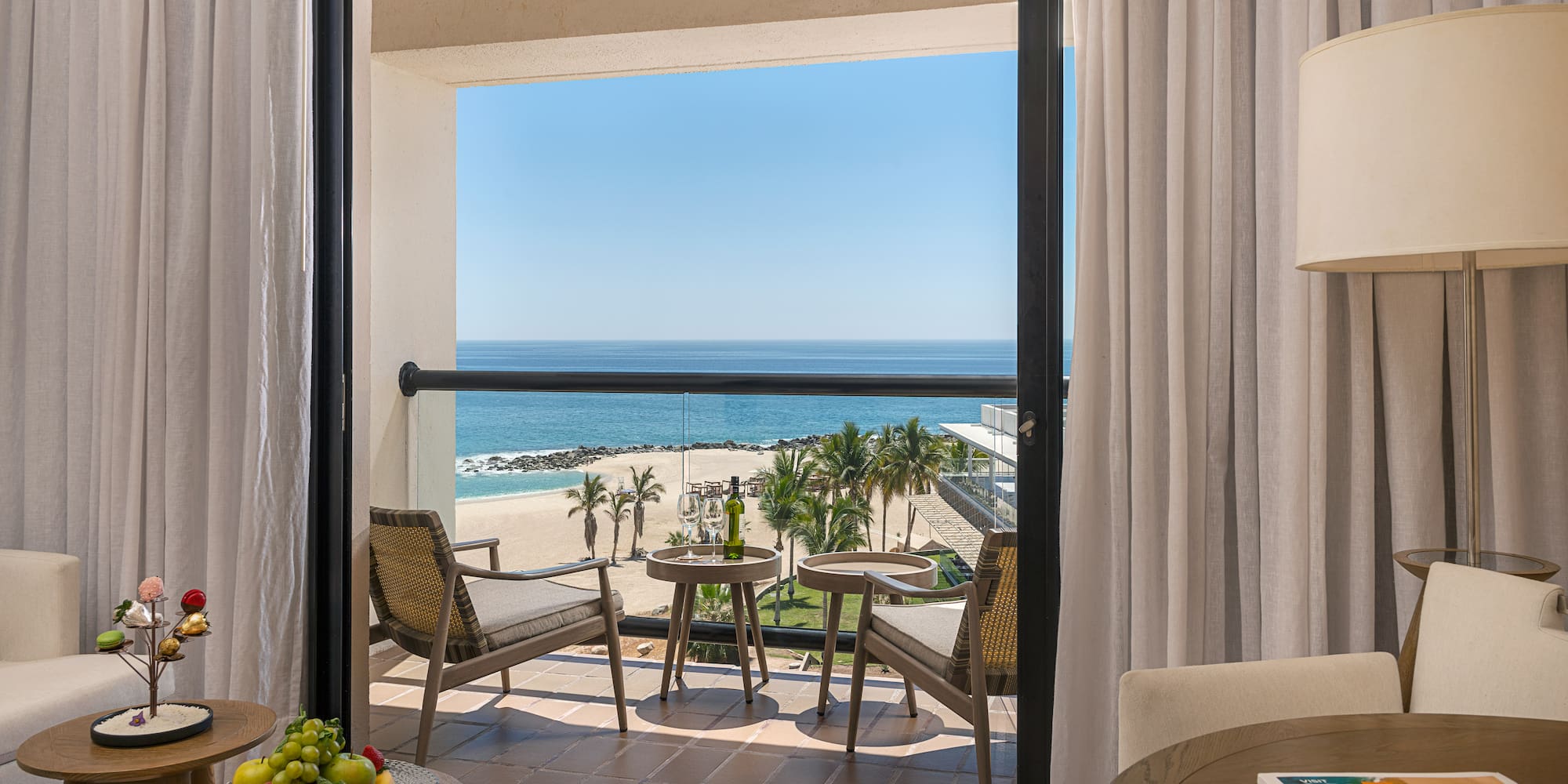 Los Cabos hotel balcony with ocean view, beach, palm trees, and wine.