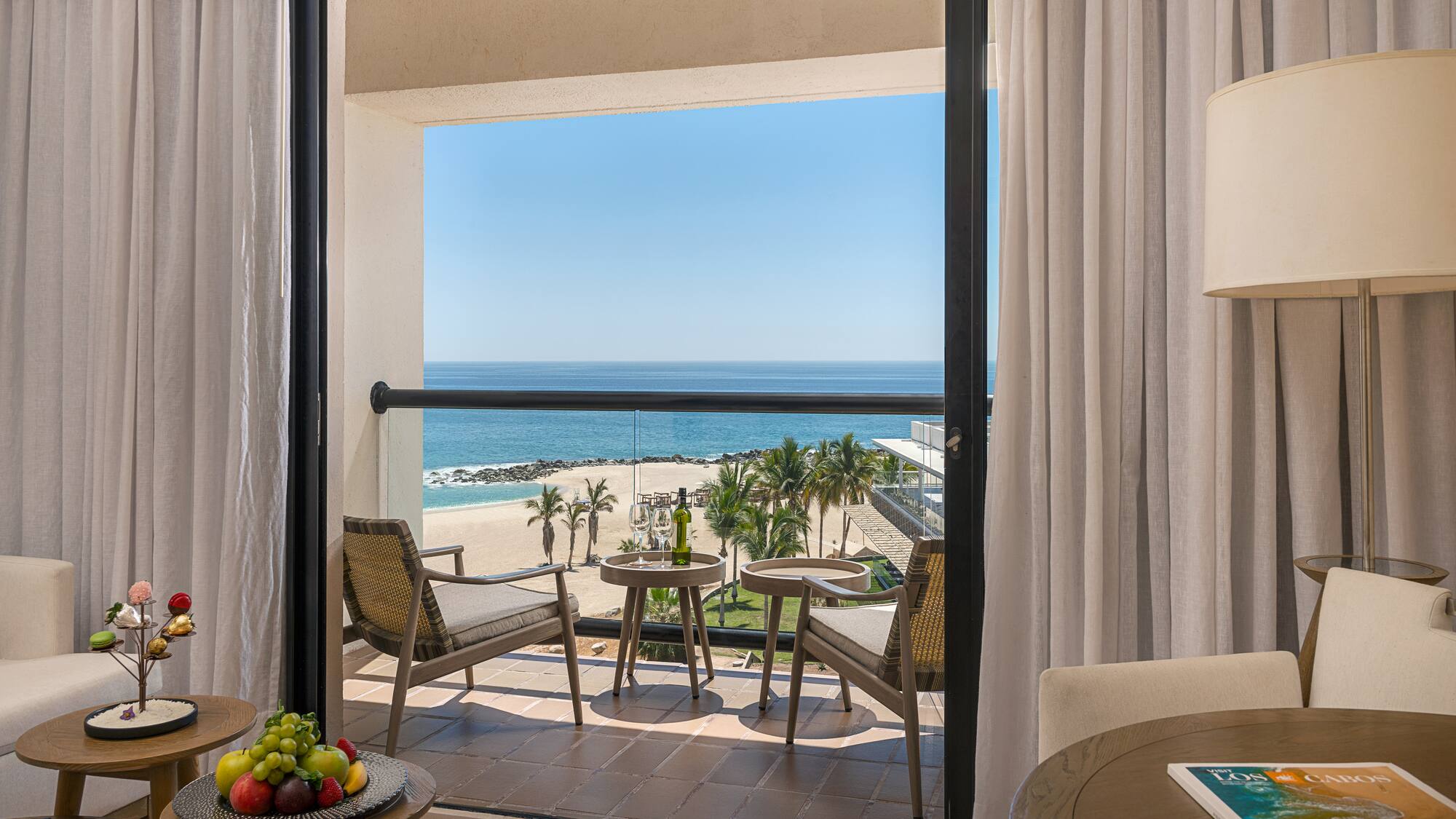 Los Cabos hotel balcony with ocean view, beach, palm trees, and wine.