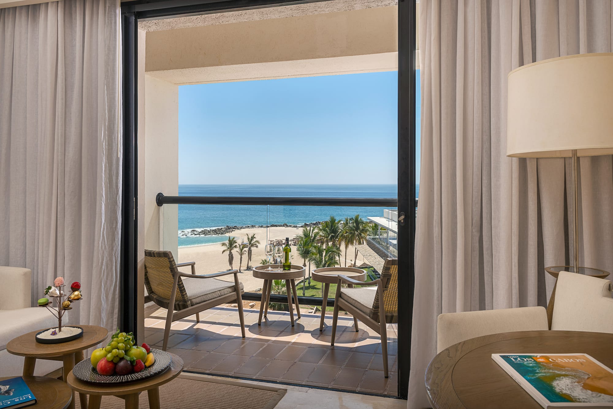 Los Cabos hotel balcony with ocean view, beach, palm trees, and wine.
