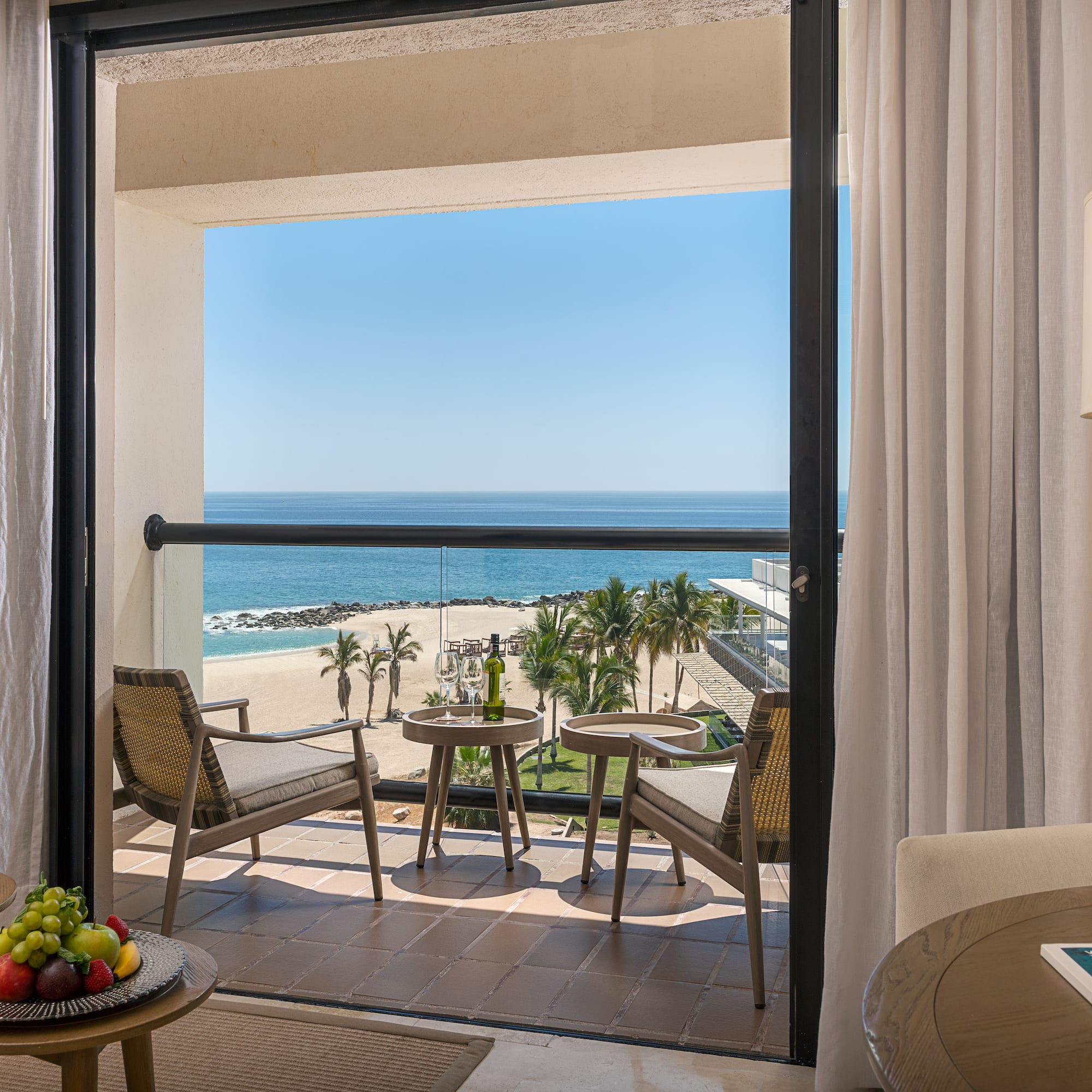 Los Cabos hotel balcony with ocean view, beach, palm trees, and wine.