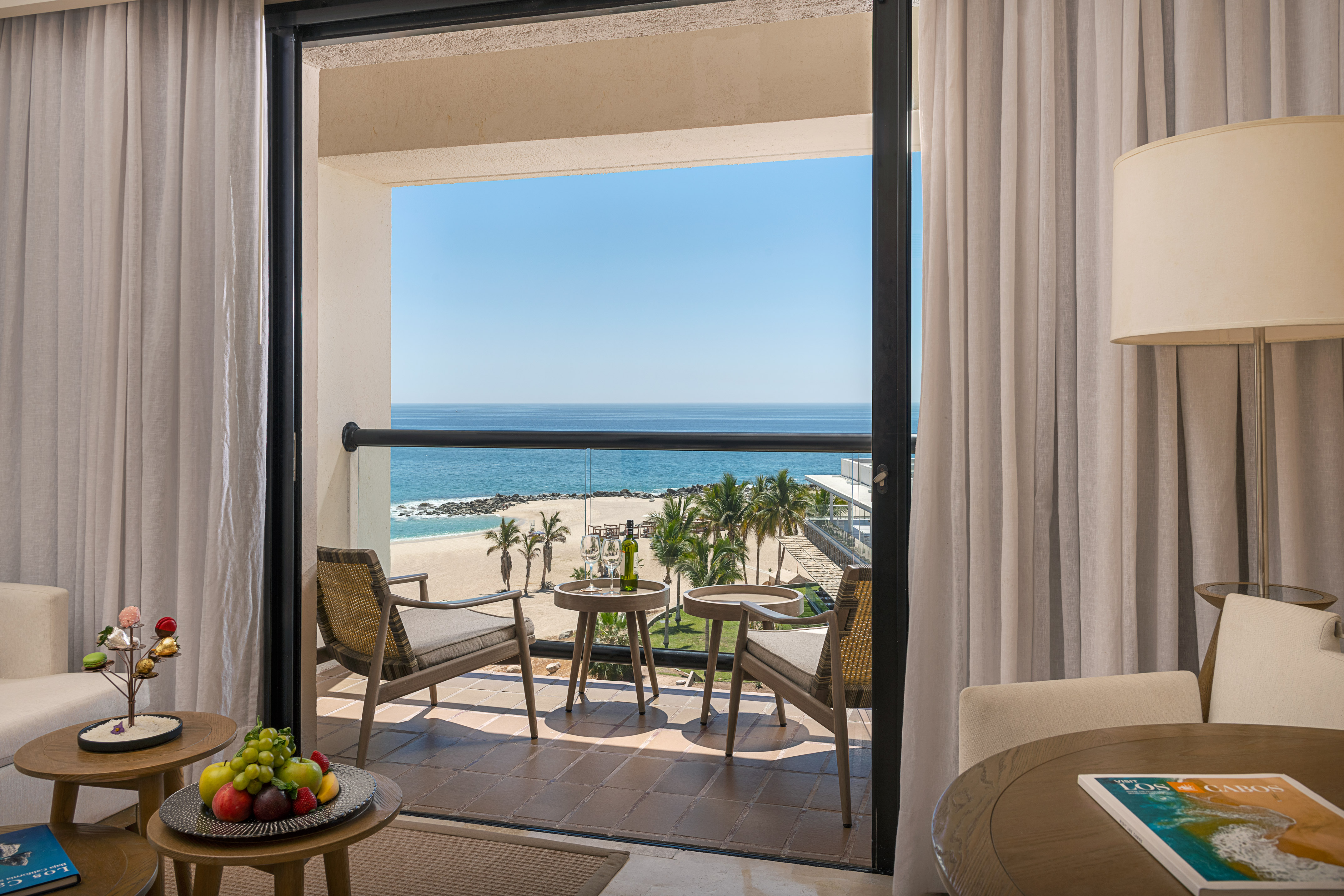 Los Cabos hotel balcony with ocean view, beach, palm trees, and wine.