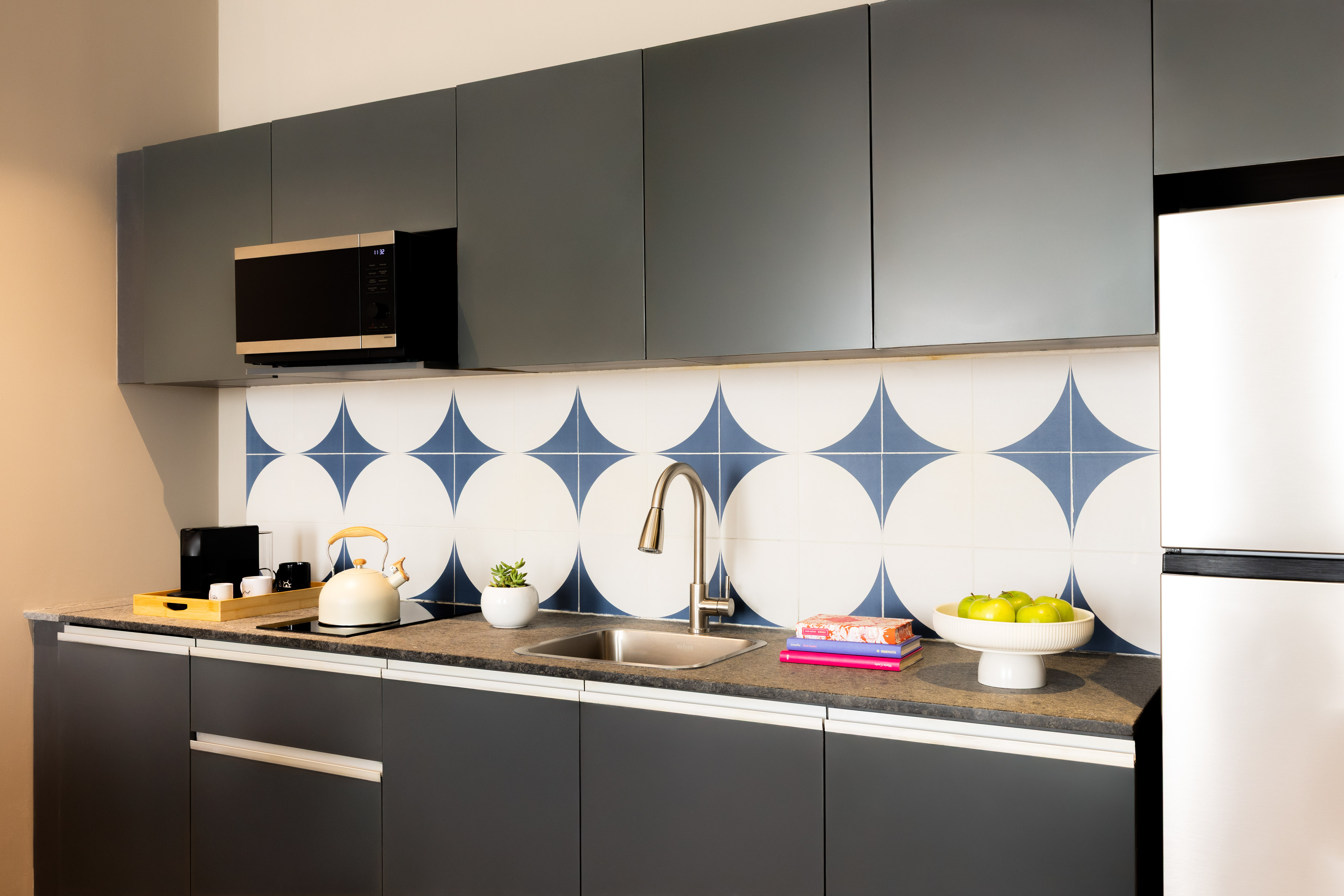 Modern grey kitchen with blue geometric tile backsplash, sink, and microwave.