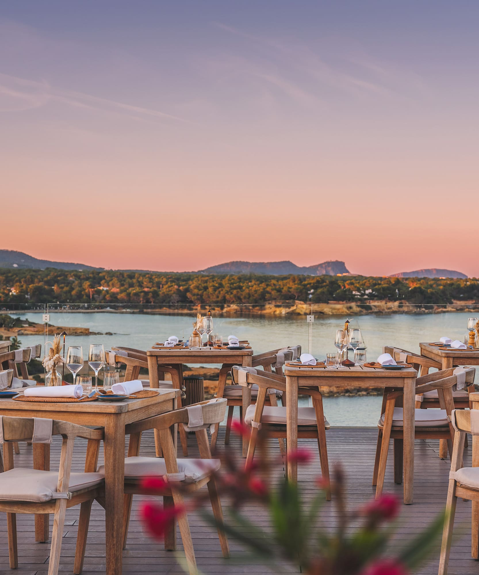 Outdoor dining terrace with wooden tables overlooking a calm sea sunset.