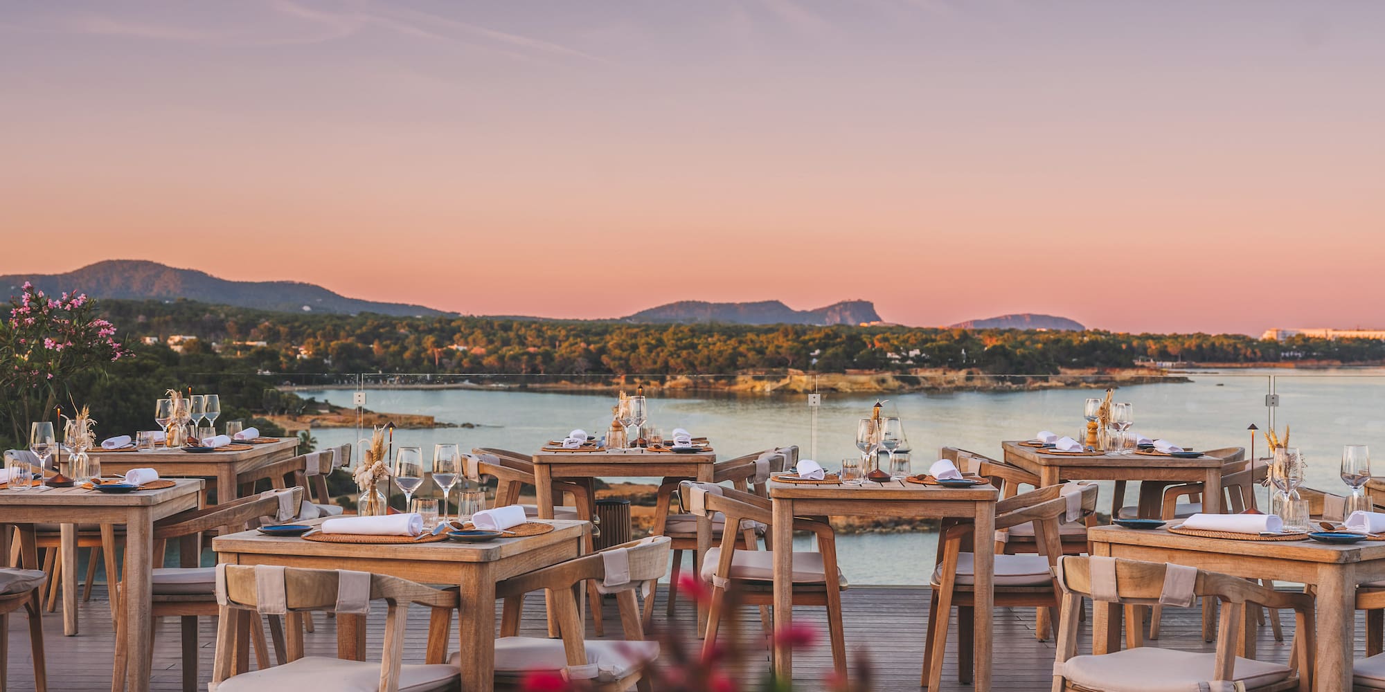 Outdoor dining deck overlooking sunset ocean with set tables.