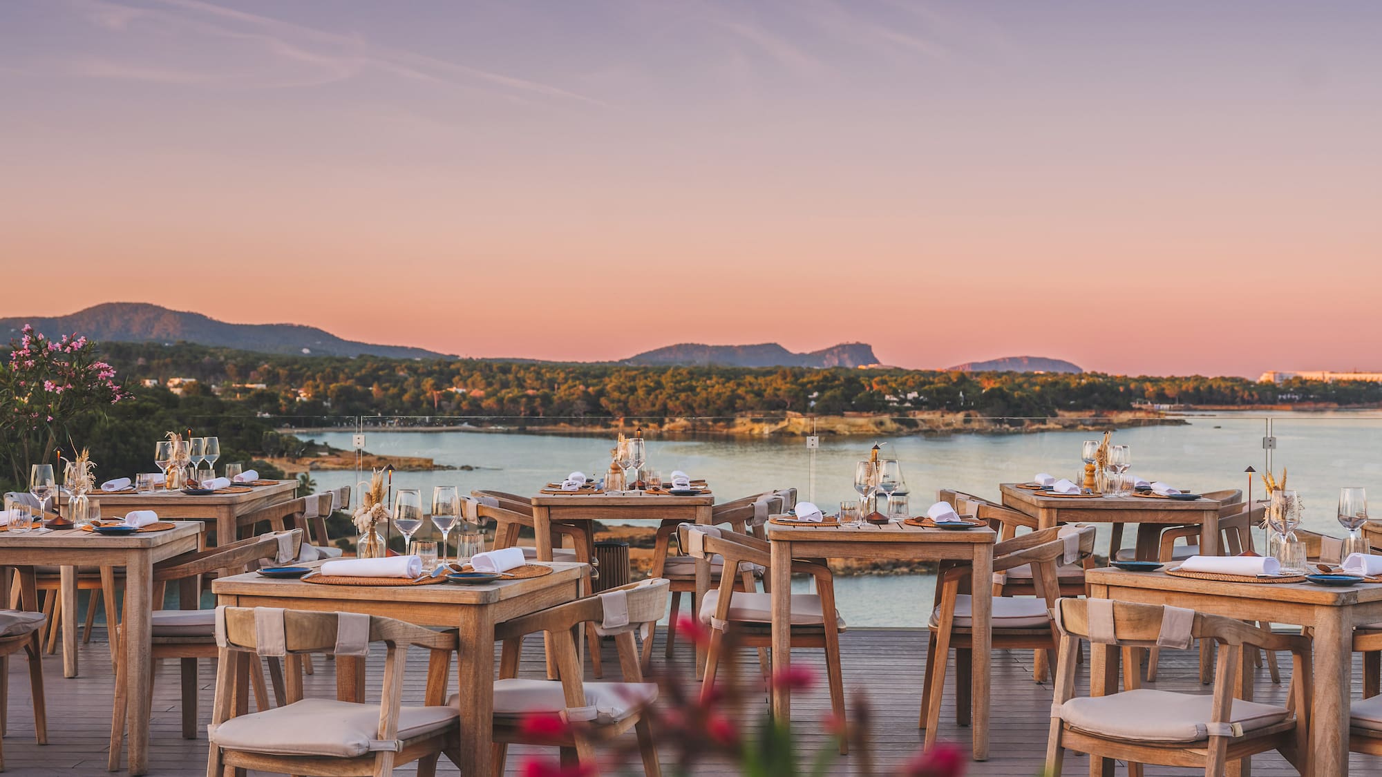 Outdoor dining deck overlooking sunset ocean with set tables.