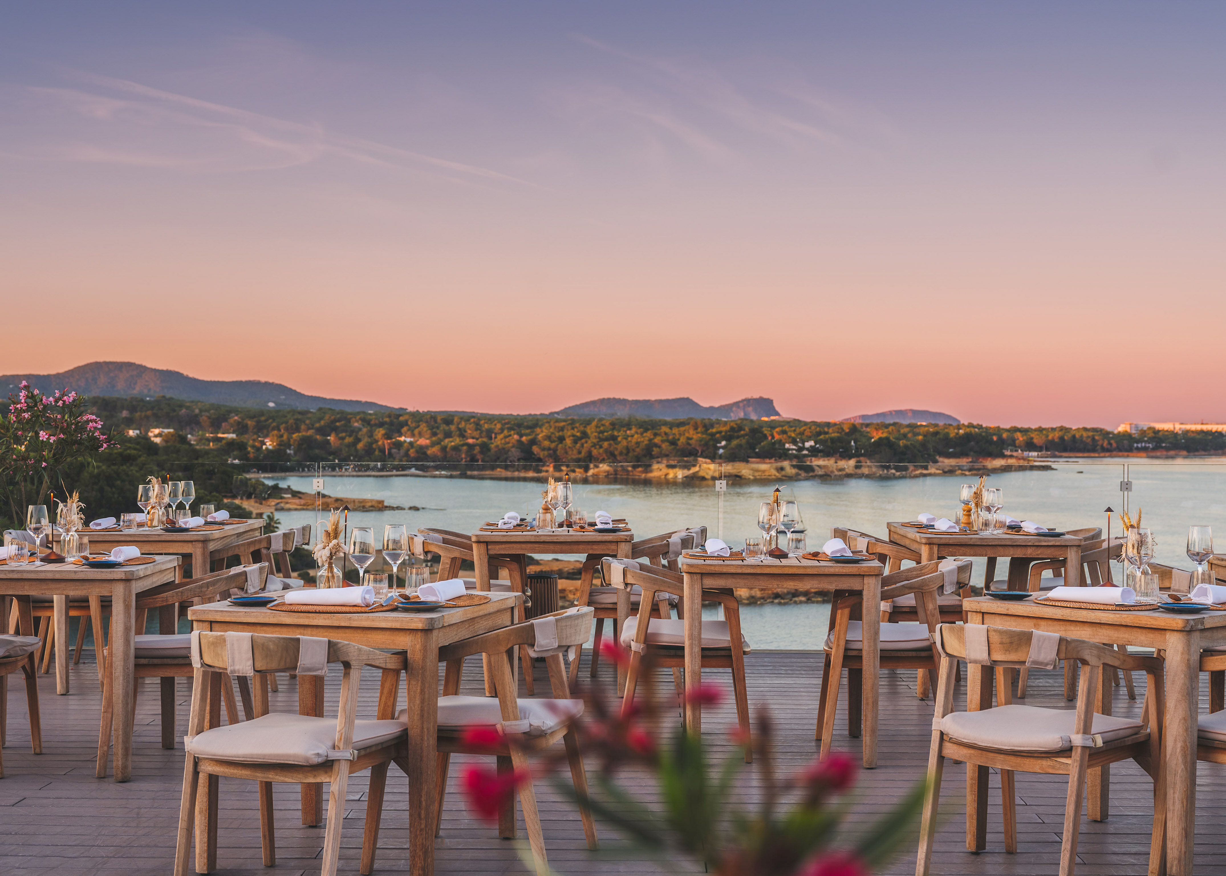 Outdoor dining deck overlooking sunset ocean with set tables.