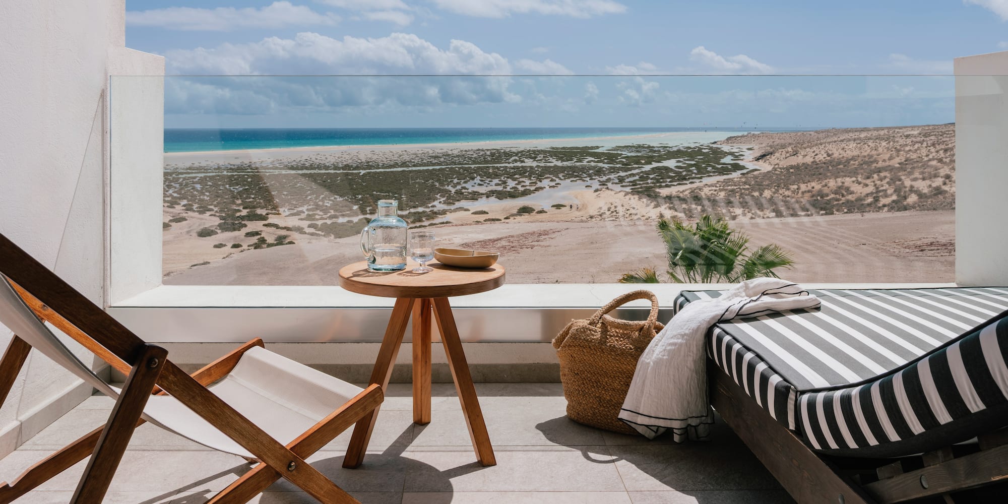 Beachfront balcony with lounge chair, table, ocean, and sandy coastline.