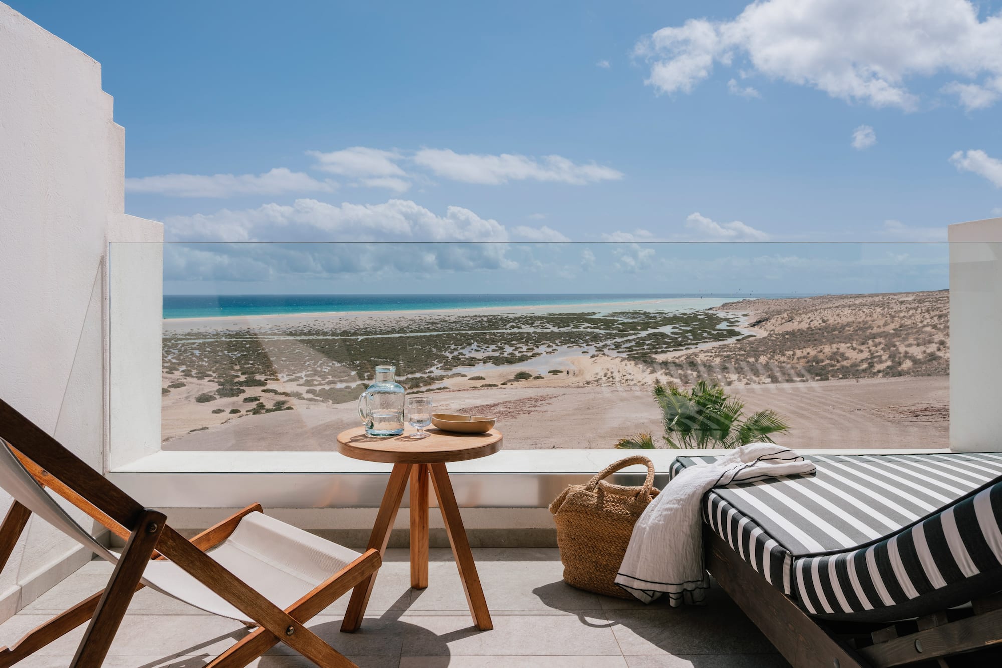 Balcón con vistas a playa desértica y mar. Tumbonas y mesa. Relax exterior.