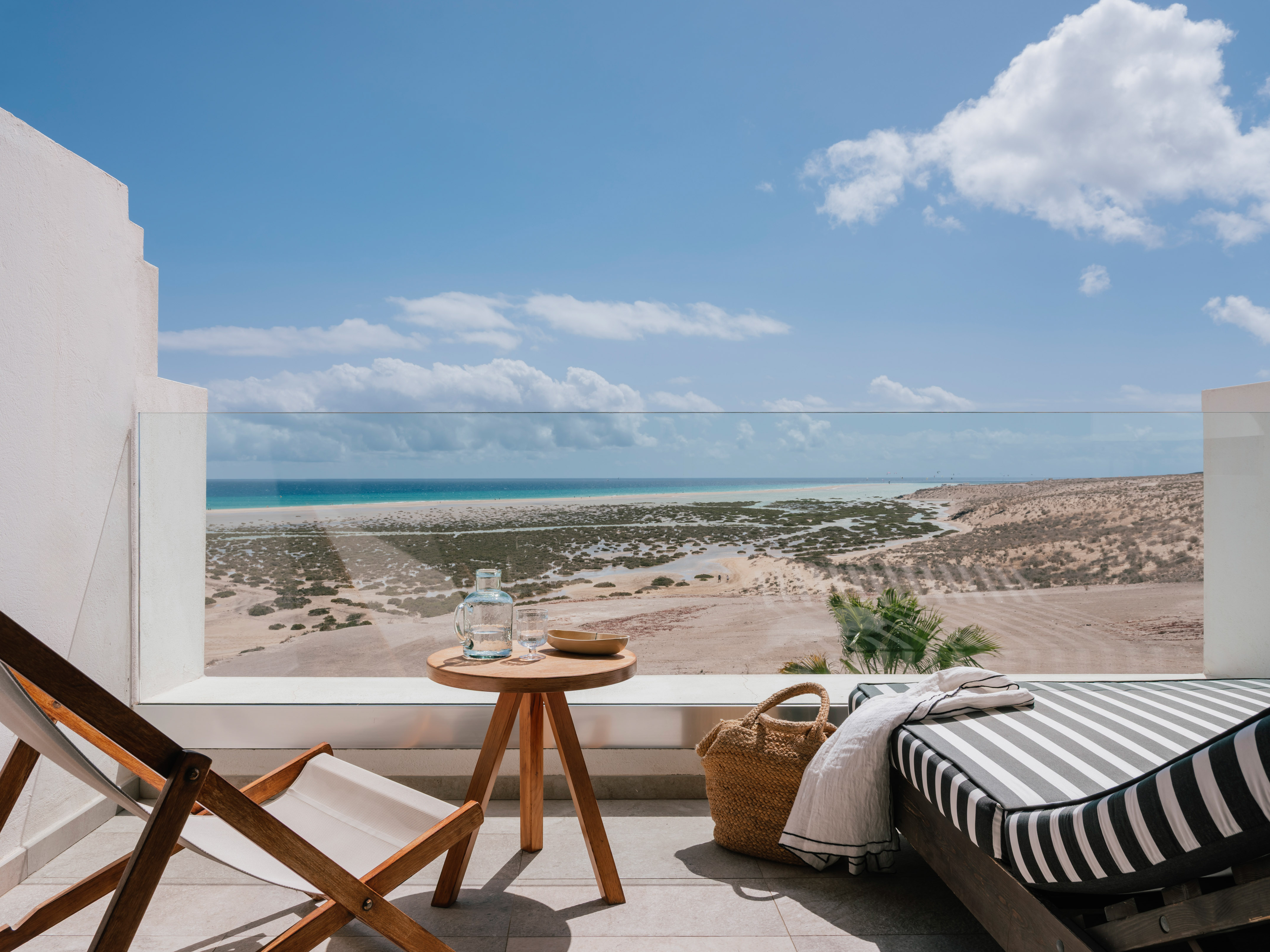 Beachfront balcony with lounge chair, table, ocean, and sandy coastline.