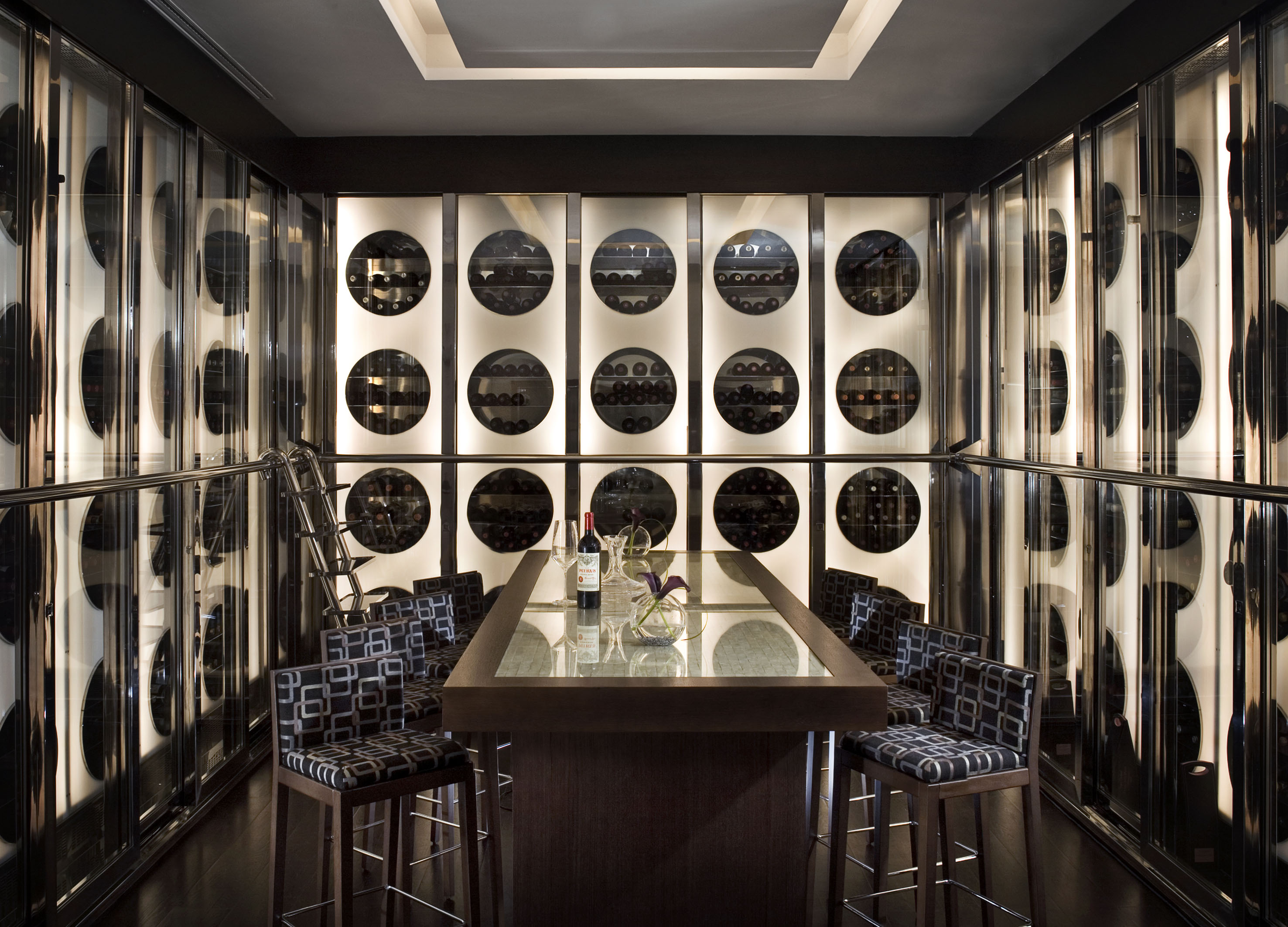 Modern wine cellar with circular glass wine racks, tasting table, and bar stools.